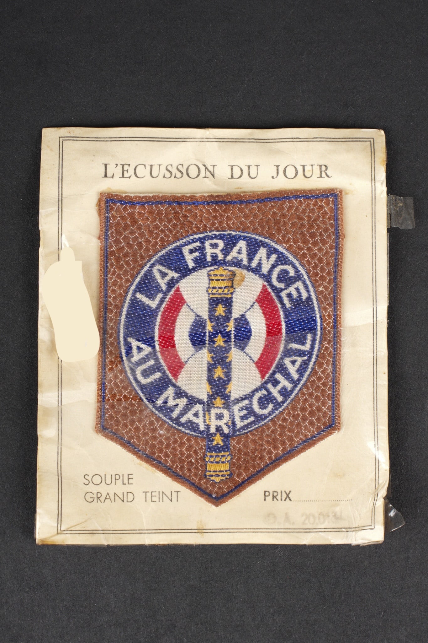 Insigne La France au Marechal. La France au Marechal badge: Insigne La France au Marechal. Insigne tisse sur fond marron sur lequel se trouve representee une Francisque tricolore portant la devise La France Au Marechal . L insigne se trouve sur son carton d or