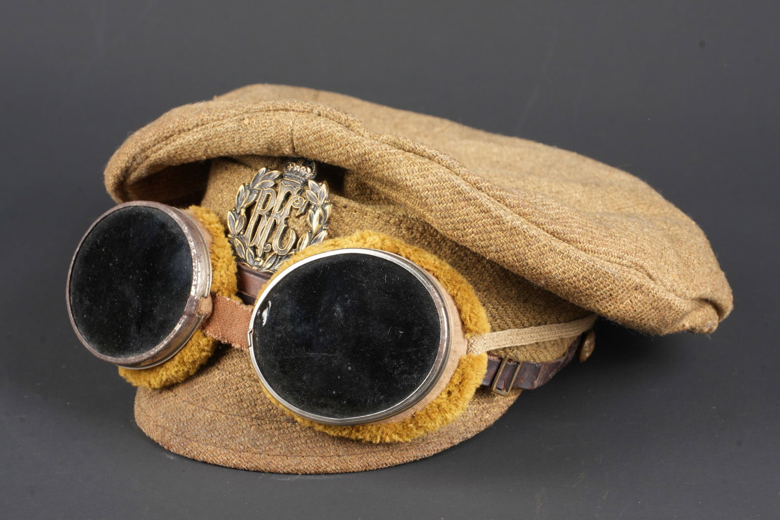 Casquette anglaise Royal Flying Corps et lunettes. British Royal Flying Corps cap and goggles: Casquette anglaise en drap avec insigne Royal Flying Corps et lunettes. Casquette souple en drap khaki, deux petits aerateurs en laiton de part et d autre. Visiere carton gainee de drap, avec 3 arcs d
