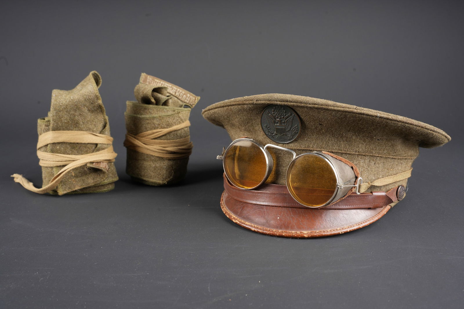 Casquette US ww1. WW1 US army cap. British and American trench lighters.: Casquette US ww1 avec bandes molletieres et lunettes. Casquette en drap khaki, insigne de type general circulaire. Oeillets aerateurs sur les cotes. Visiere en cuir marron doublee de basane verte au