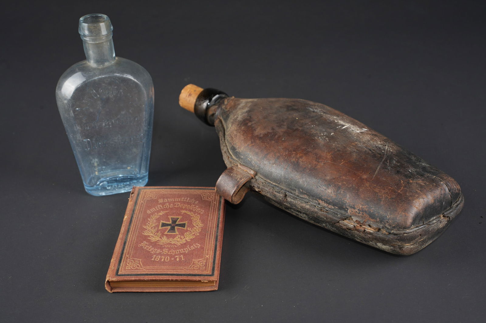 Equipement allemand 1870. German equipment, 1870 period: Gourde, et souvenirs allemands Guerre de 1870 jusque 1888. Gourde en verre gainee de cuir avec un passant de chaque cote. Bouchon non d origine. Une bouteille en verre marquee Andenken an meine Dienst