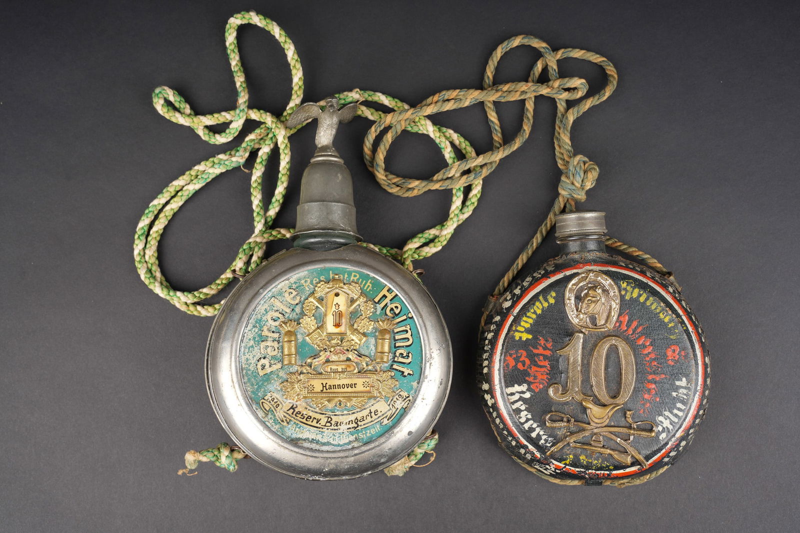 Lot de 2 gourdes de reserviste du FAR10 de Hanovre et du Dragoner Rgt Nr 10. two reservist canteens: Lot de 2 gourdes de reserviste du FAR10 de Hanovre et du Dragoner Rgt Nr 10. Gourde du FAR10 avec ses bouchons et son cordon. Au dos un couvercle porte cigarettes, mecanisme de blocage defaillant. Un