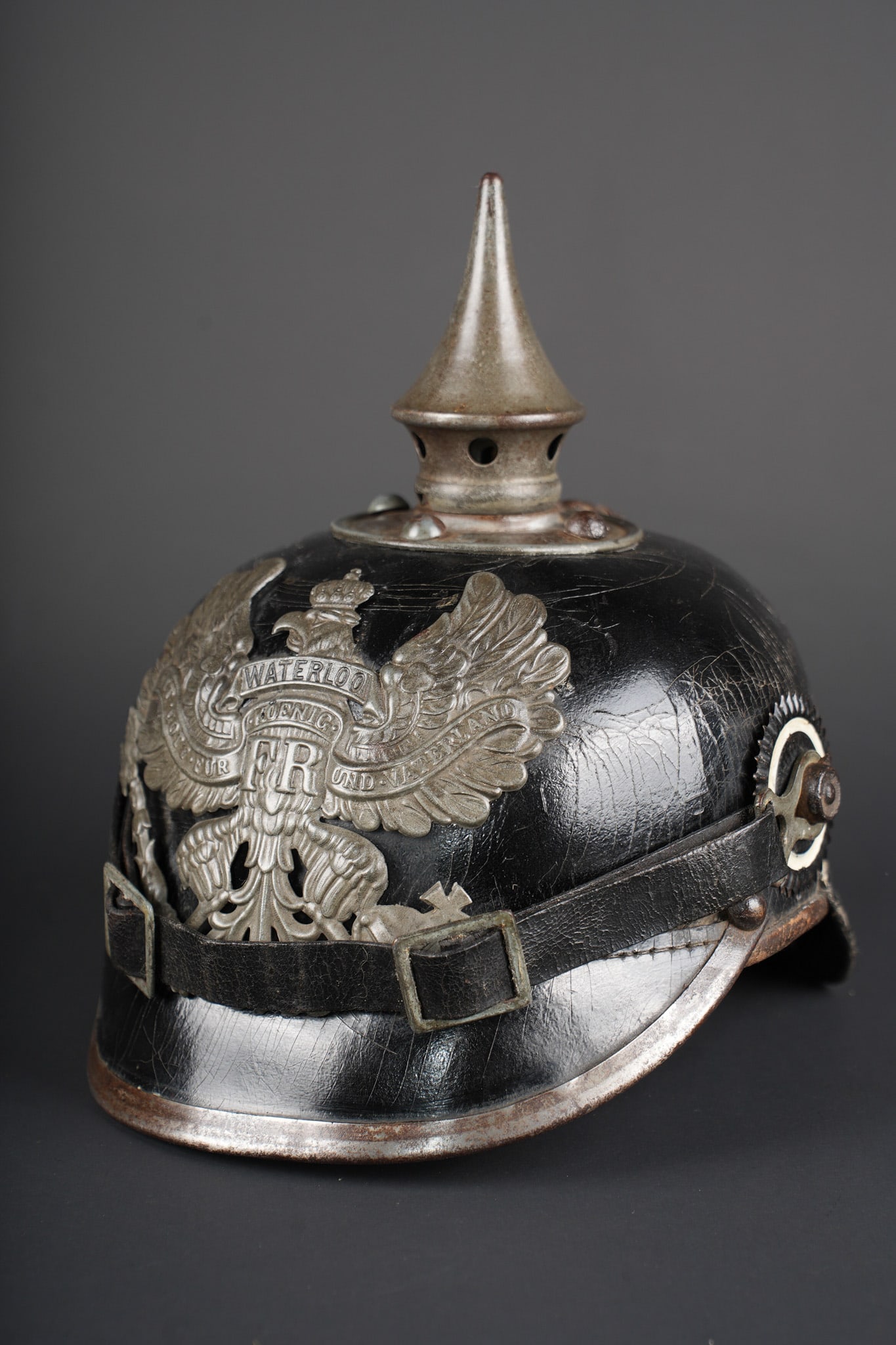 Casque a pointe M1915 troupe du Hanovre. Hanoverian enlisted M1915 pickelhaube: Casque a pointe M1915 troupe du Hanovre. Bombe en cuir non repercee. Pas de marquage visible. Garnitures fer peintes feldgrau. Plaque monobloc a banderole WATERLOO, pontets soudes d origine et belle