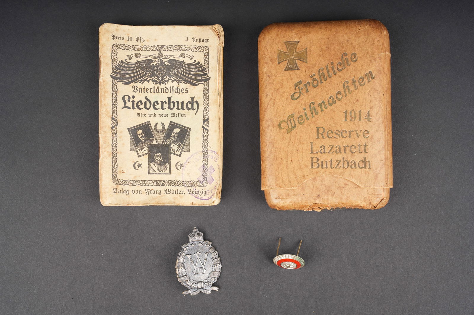 Hesse cocarde, etui a cigares et insigne. Hessian cockade, cigar case and badge: Hesse cocarde, etui a cigares et insigne. Un etui a cigares Noel 1914 du Reserve Lazarett de Butzbach, contenant un livret de chants. Un insigne de veteran JR186, R116, R222, R254 et Landwehr116. Une