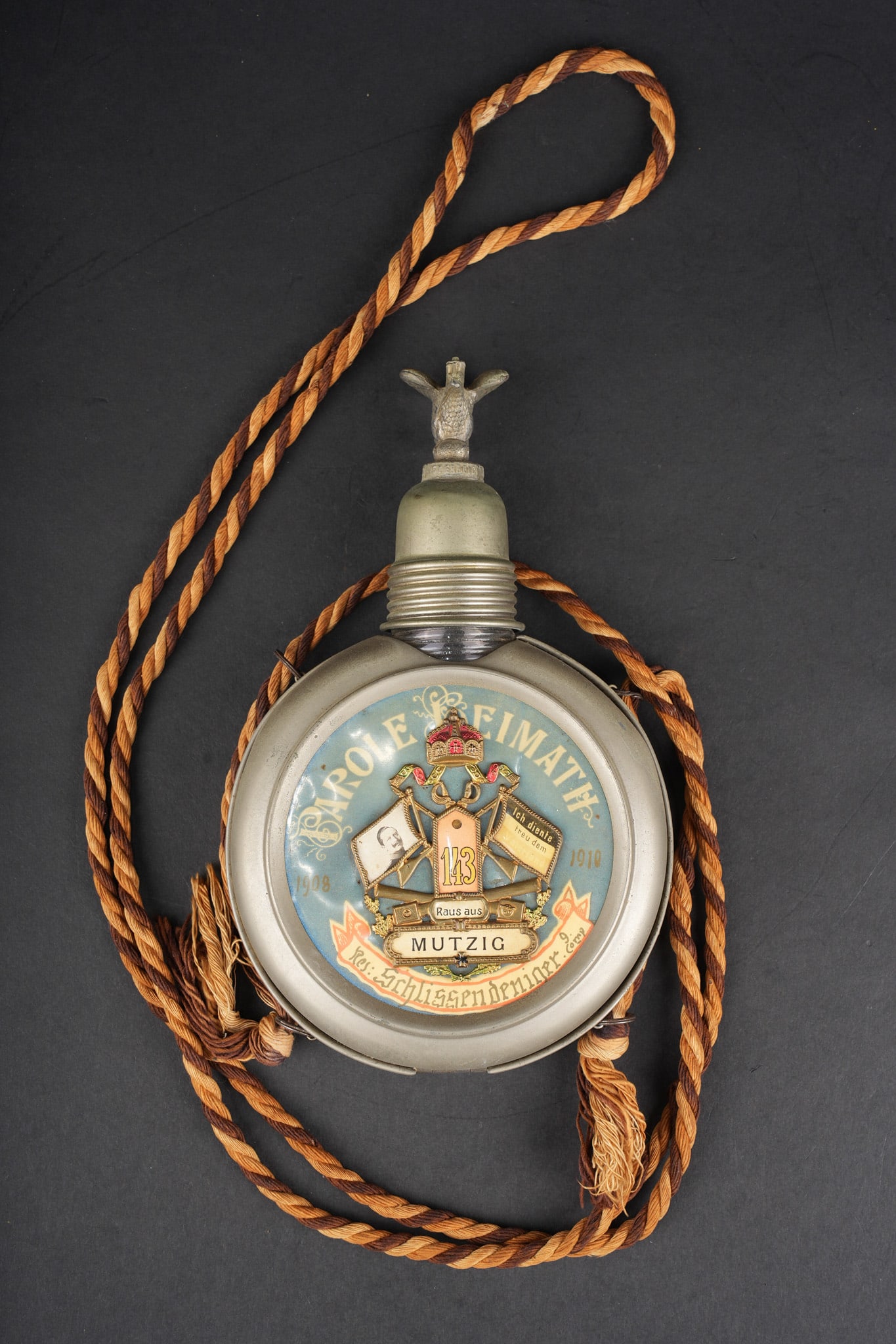 Gourde de reserviste du JR143 de Mutzig. Reservist canteen of Infantry Regiment JR 143, Mutzig: Gourde de reserviste du JR143 de Mutzig. Gourde en verre en bon etat, avec ses bouchons, dans sa coque en fer blanc. Motif patte d epaule du JR143 de Mutzig, 9e Kompanie. Avec son cordon tricolore. Us