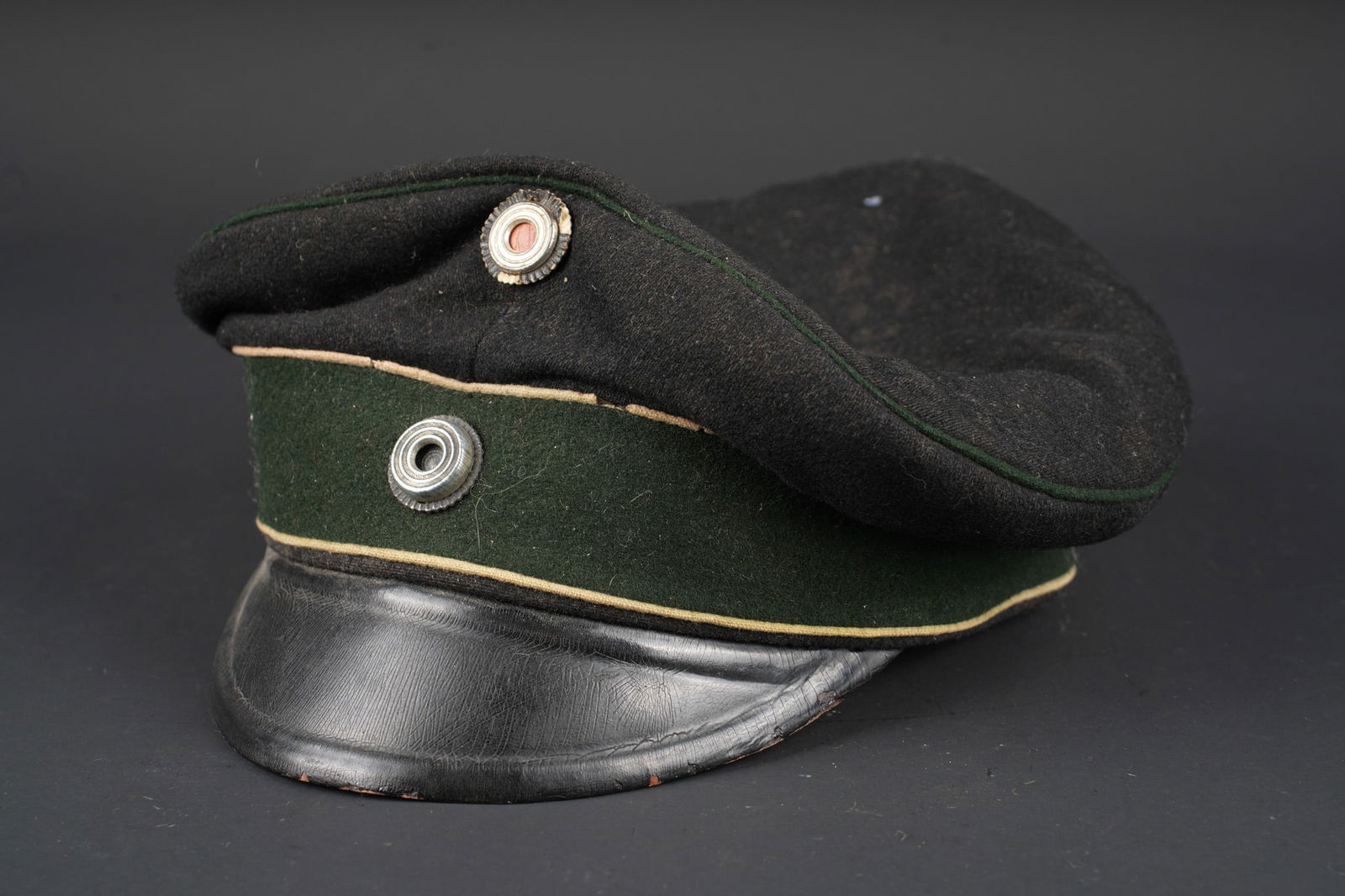 Casquette imperiale allemande. Imperial German visor cap: Casquette imperiale allemande. Schirmmutze imperiale en drap noir, passepoil superieur vert fonce, bandeau vert fonce a deux passepoils blancs. Cocardes type officier dont landcocarde prussienne. Corp