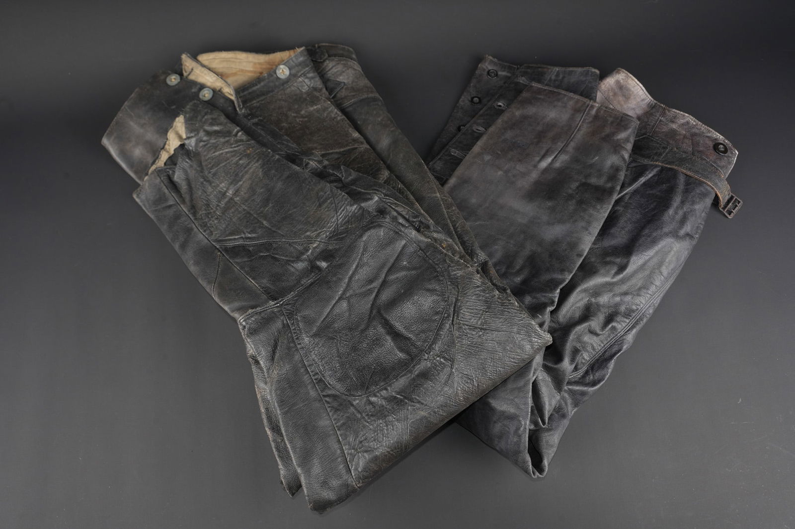 Lot de 2 pantalon-culottes en cuir. Lot of two leather riding breeches.: Lot de 2 pantalon-culottes en cuir. Post-1918. Une culotte en cuir de motard avec renforts ou reparations aux genoux, montee avec des boutons allemands et ayant recu une reproduction de tampon a l