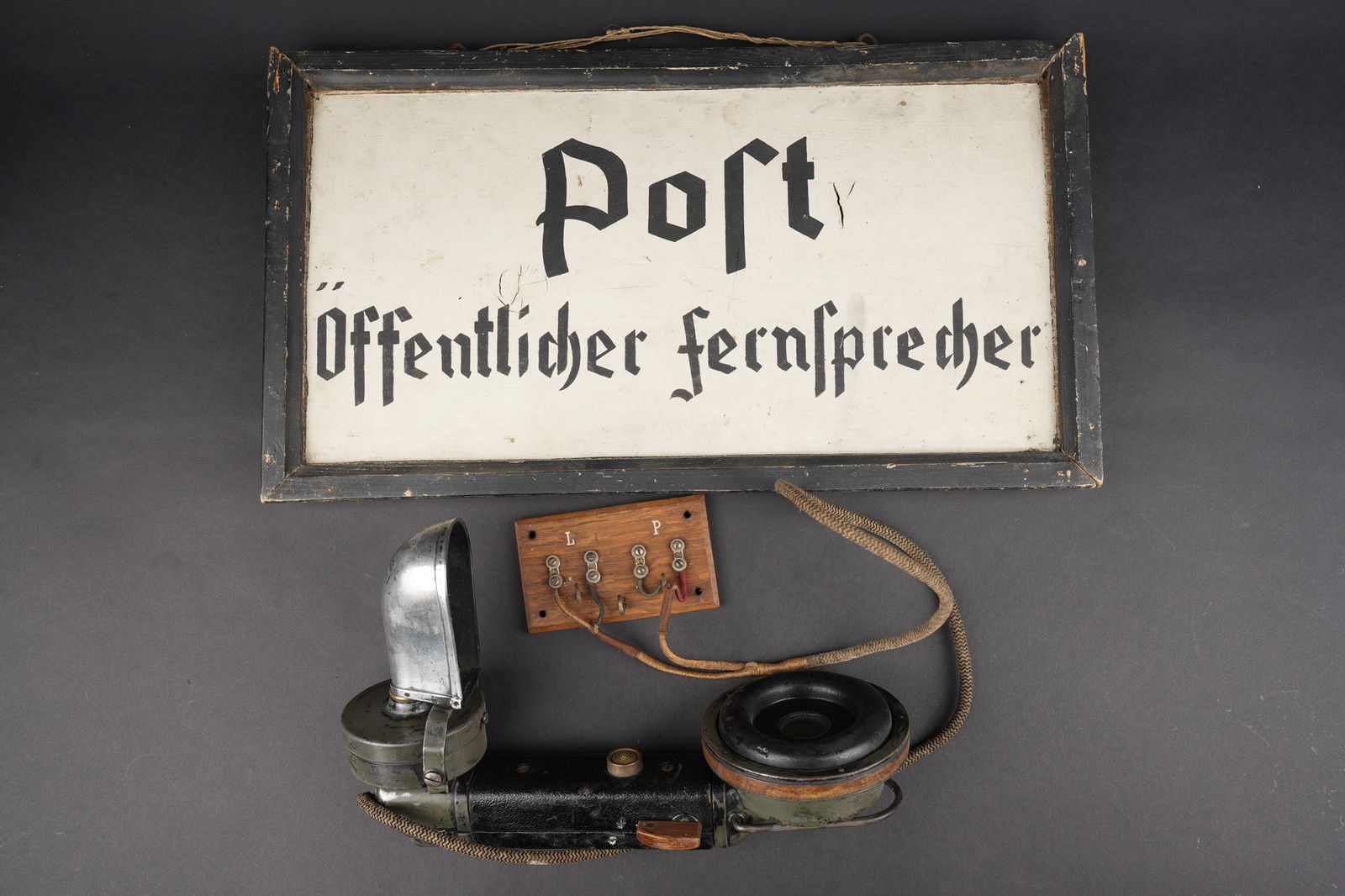 Combine telephonique allemand et panneau. German telephone handset with signal panel.`: Combine telephonique allemand et panneau. Un combine telephonique allemand, cable branche sur une planchette bois, bon etat general. Un panneau en bois peint Post offentlischer Fernsprecher, environ 4