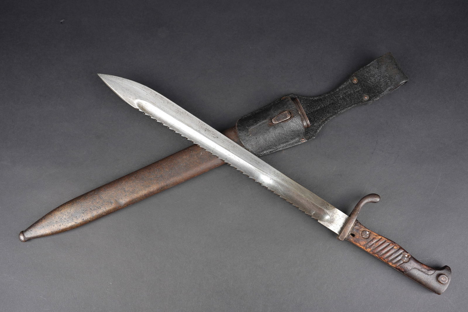 Baionnette 98-05 a dents de scie avec porte fourreau. Seitengewehr 98/05 with sawback blade and: Baionnette 98-05 a dents de scie avec porte fourreau. Belle lame du fabricant Haenel datee 1916. Plaquettes bois usees, poussoir a debloquer. Fourreau fer. Porte fourreau en cuir cire noir. Usure d us