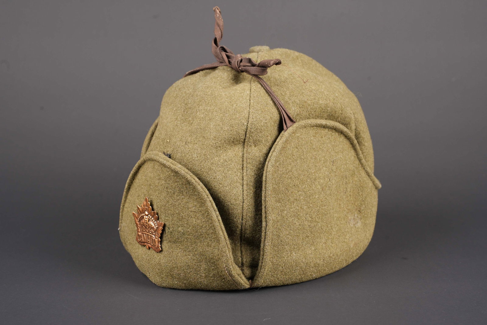Bonnet canadien. Canadian cap.: Bonnet canadien. En epais drap kaki. Les sangles de maintien des rabats sont presentes, mais partiellement effilochees. Interieur double en tissu molletonne noir. Reste d insignes illisibles. Taille 7