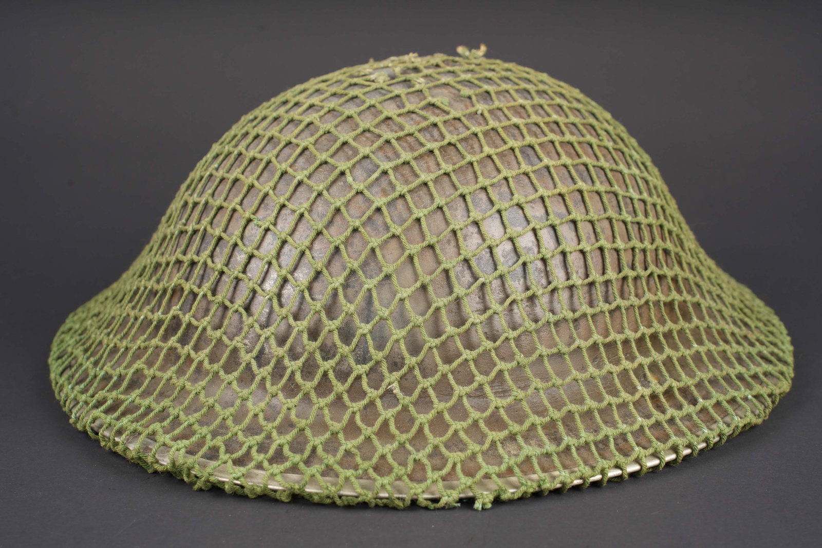 Casque britannique. British MK II helmet.: Casque britannique. Coque de casque MKII, fortement usee et oxydee. Filet de camouflage en cordelette verte. Cordon de serrage present, mais posterieur. Coiffe incomplete avec d importants manques. Ju
