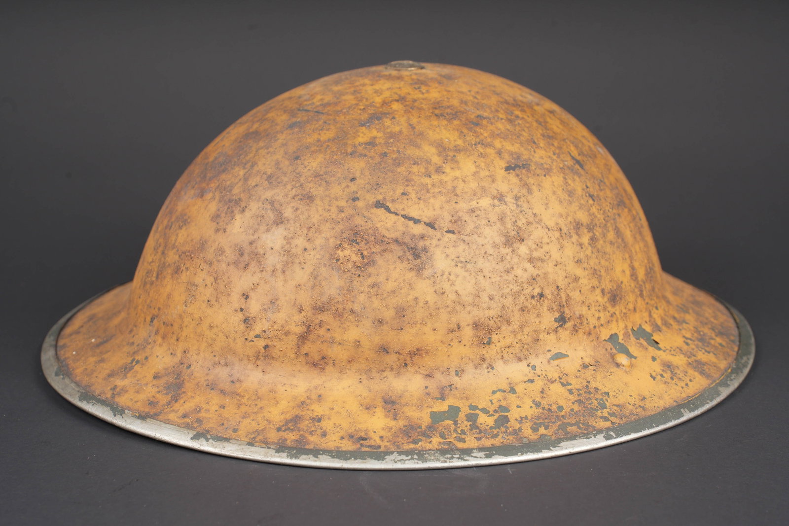 Coque de casque MK II. British Mk II helmet shell: Coque de casque MKII. Coque de casque en metal. Peinture jaune sable a 70%. Couleur fortement vieillie par le temps. Coiffe absente. Le boulon de fixation est present. Interieur de la coque oxyde. Jug