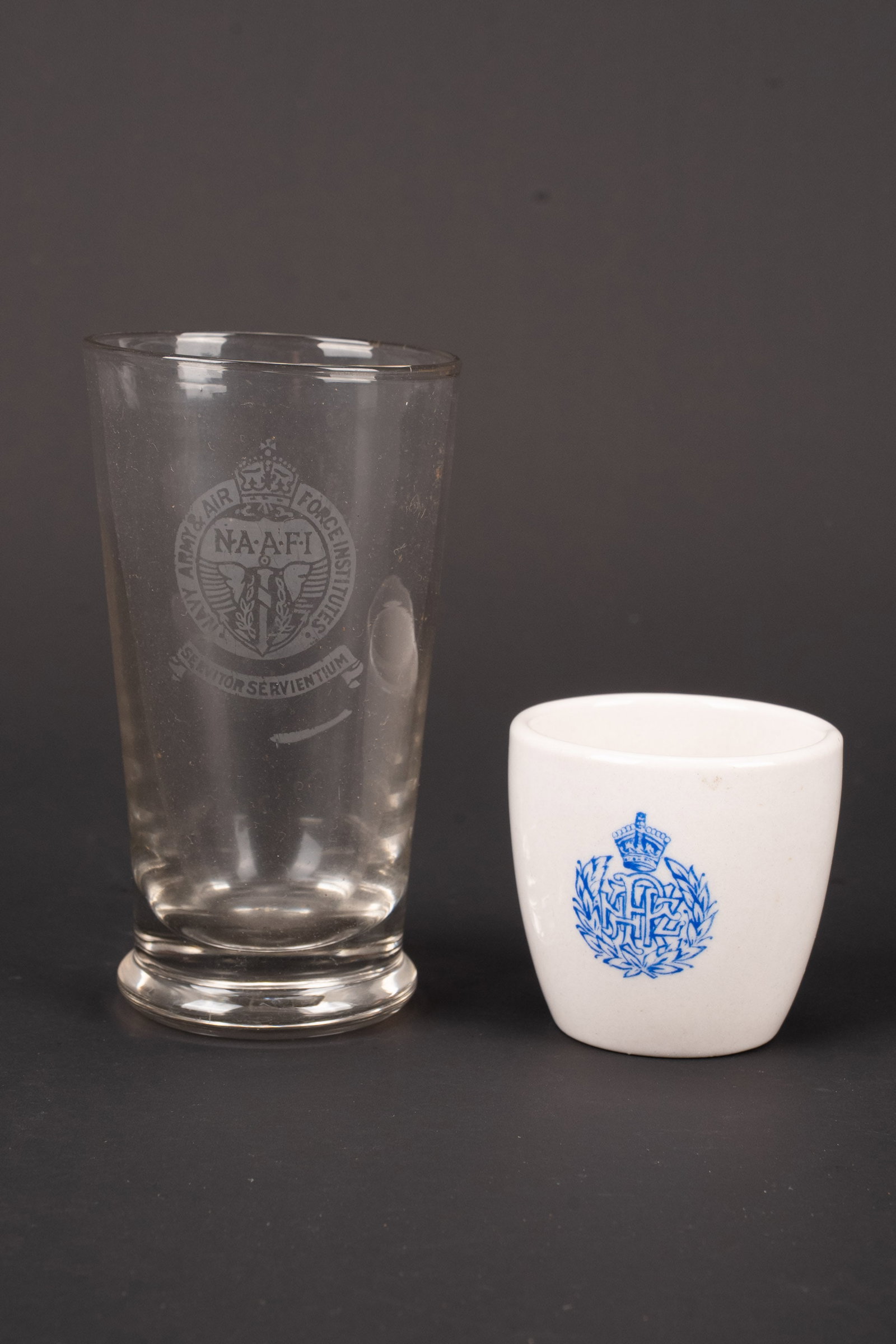 Vaisselle NAAFI. NAAFI tableware: Vaisselle NAAFI. Comprenant un verre transparent, grave de l insigne NAAFI. Hauteur 10 cm. Une petite tasse en ceramique blanche, marquage NAAFI de couleur bleu. Marquages New Zealand. Hauteur 4,5