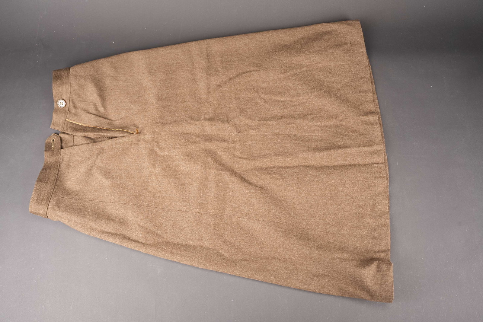 Jupe pour Waac. WAAC skirt: Jupe de Waac. En drap marron. Bouton present. Fermeture eclaire fonctionnelle. Fabrication Serval. Etiquette indiquant une taille 12. A noter une certaine usure et patine de la piece, ainsi que