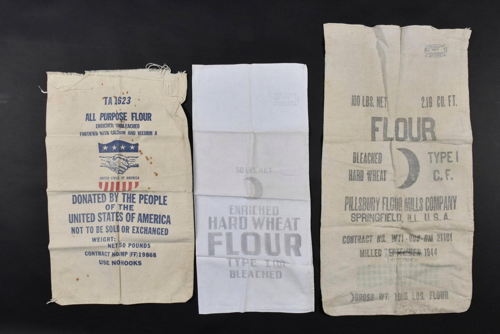 Sacs de ration US. US Army ration bags.: Sacs de ration US. Comprenant un sac en tissu coton blanc, marquage bleu TA 1623 All Purpose Flour Donated by the People of the United States of America. La partie superieure du sac est dechiree. Un s
