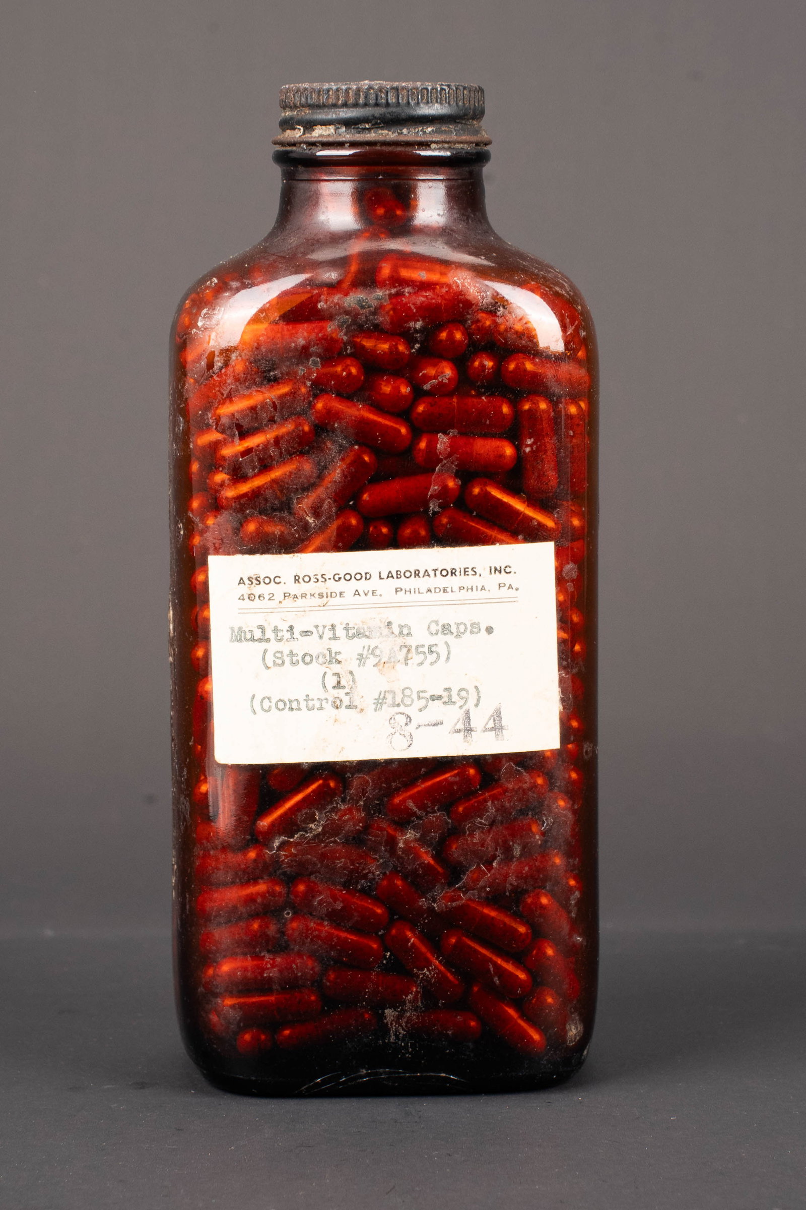 Flacon de vitamines US. US Army vitamin bottle.: Flacon de vitamines US. Bouteille complete en verre orange. Bouchon metallique present. Etiquette marquee Multi Vitamin Caps. Fabrication Assoc Ross Good Laboratories Inc Philadelphia. Datee du mois