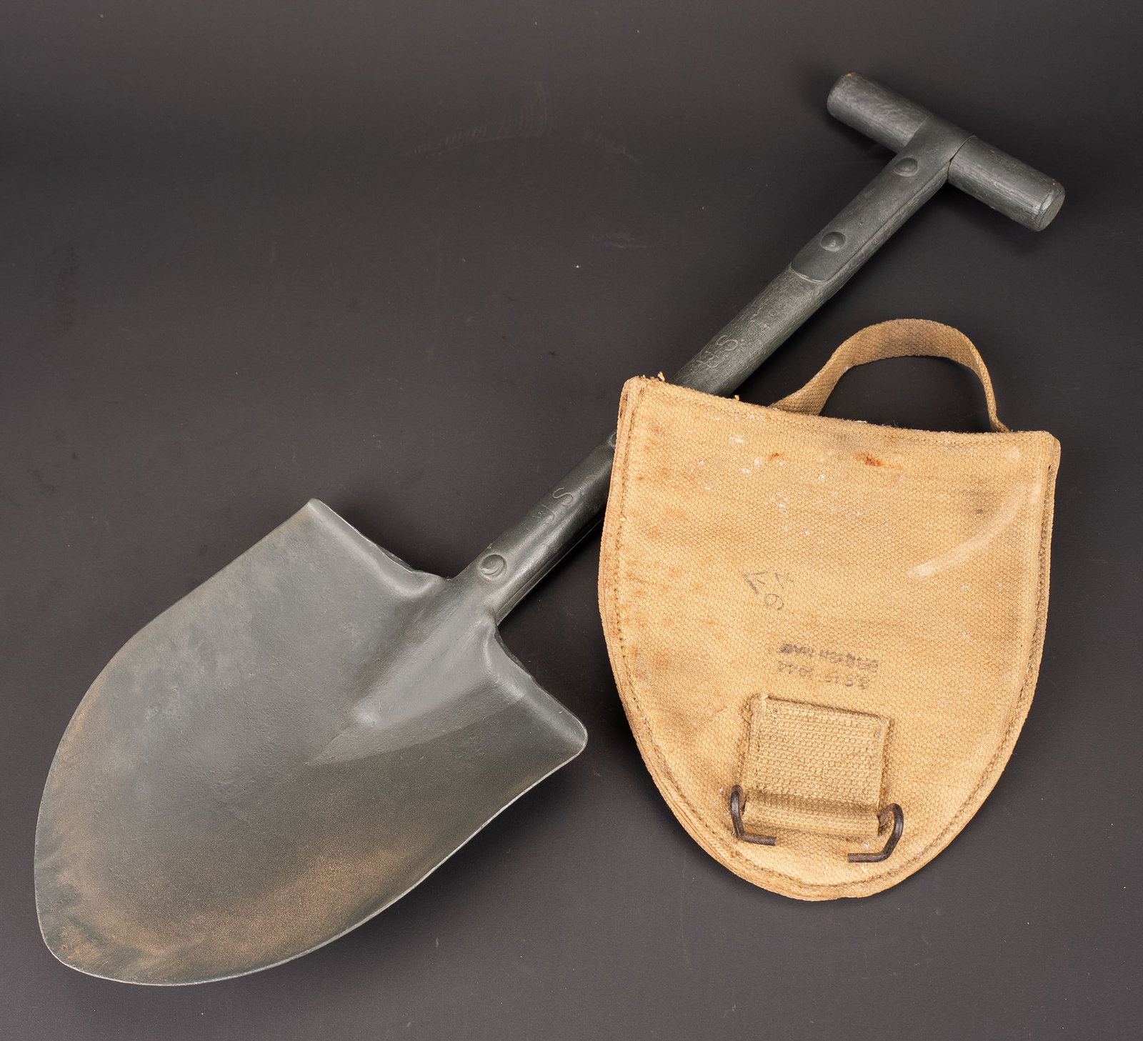 Pelle en T US. US Army T-handle shovel.: Pelle en T us. Bois et parties metalliques repeintes. Marquages US visibles. Housse en toile web British Made. Le crochet de fixation au ceinturon est present. La sangle est complete. Beau marquage