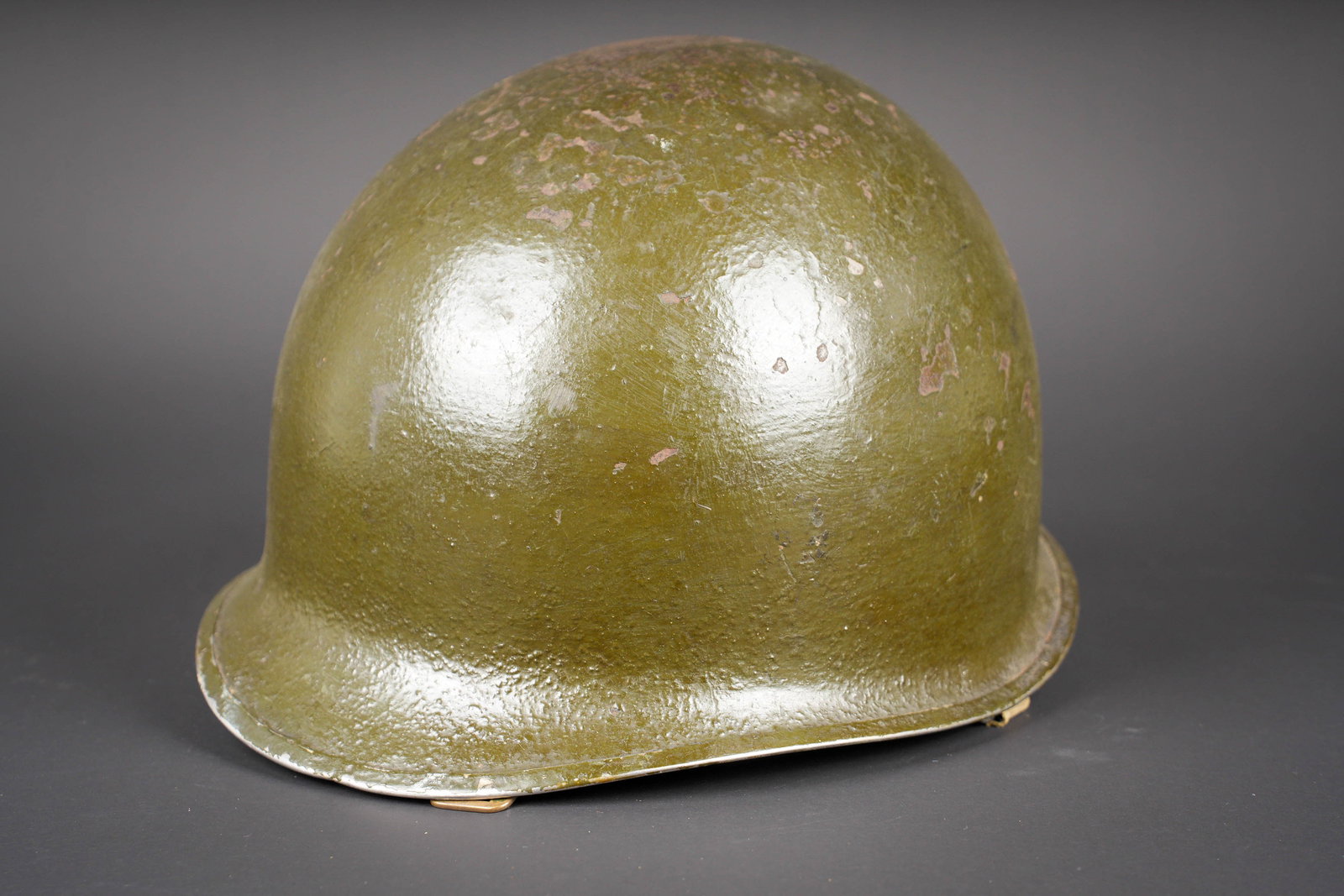 Coque de casque USM1. US M1 helmet shell.: Coque de casque USM1. En metal, fermeture du jonc a lavant. Coque repeinte. Les pontets sont fixes. Les jugulaires sont presentes et cousue dorigine. Numero de lot illisible. Laundry number Q-6880