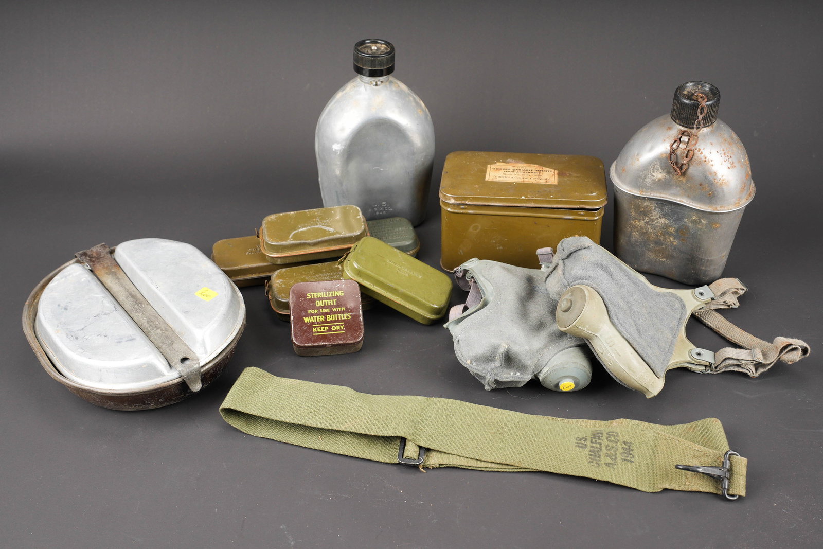Equipements US. US Army equipment.: Equipements US. Comprenant une gourde complete en metal, avec son bouchon et sa chainette, datee 1944. Deux masques anti-poussieres M1, en caoutchouc gris et feutrine grise, toutes les sangles sont pr