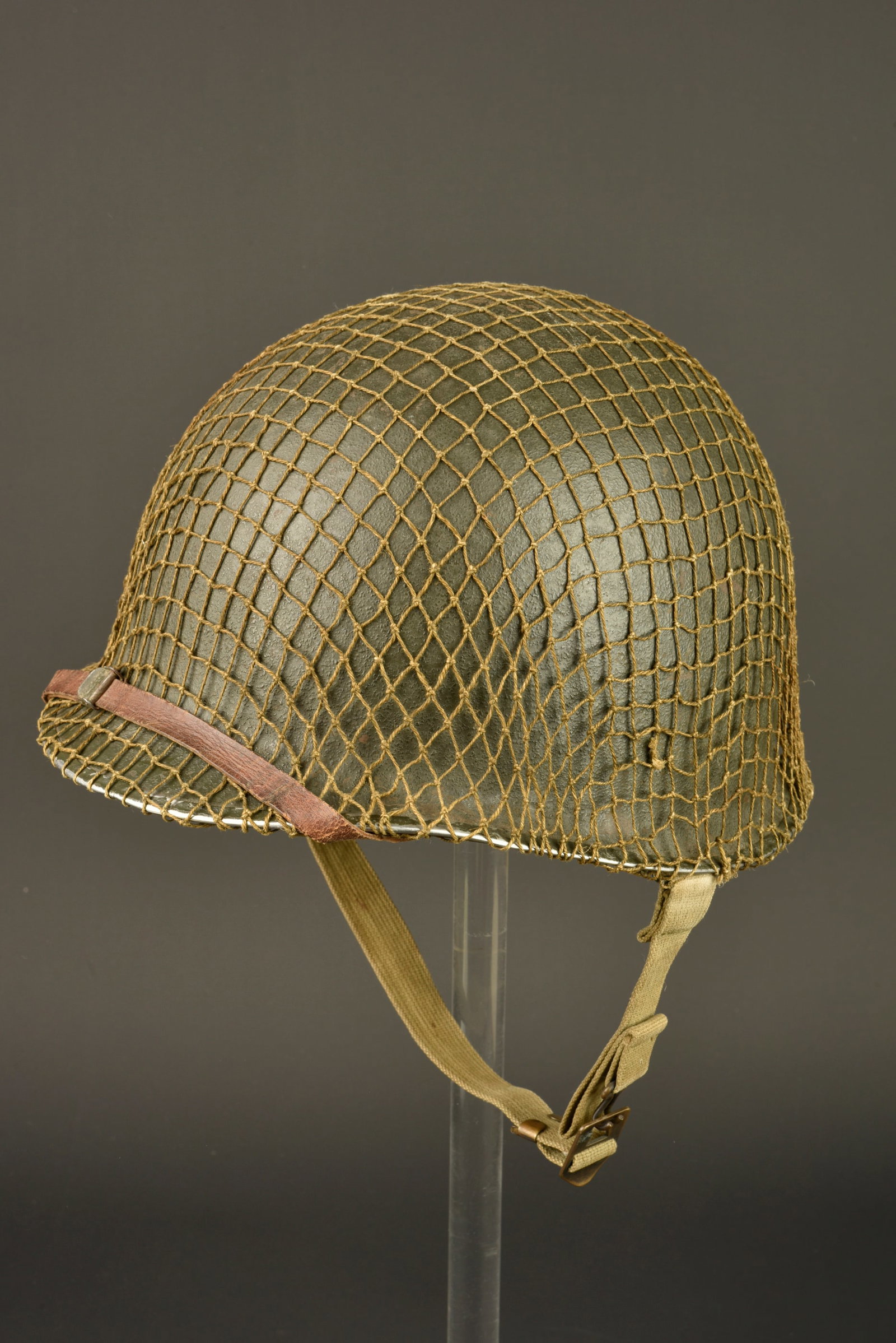 Casque USM1. USM1 Helmet.: Casque USM1. Coque de casque USM1, fermeture du jonc a lavant. Numero de lot illisible. Pontets fixes. Les jugulaires sont completes et montees dorigine. Filet de camouflage petites mailles. Peinture 