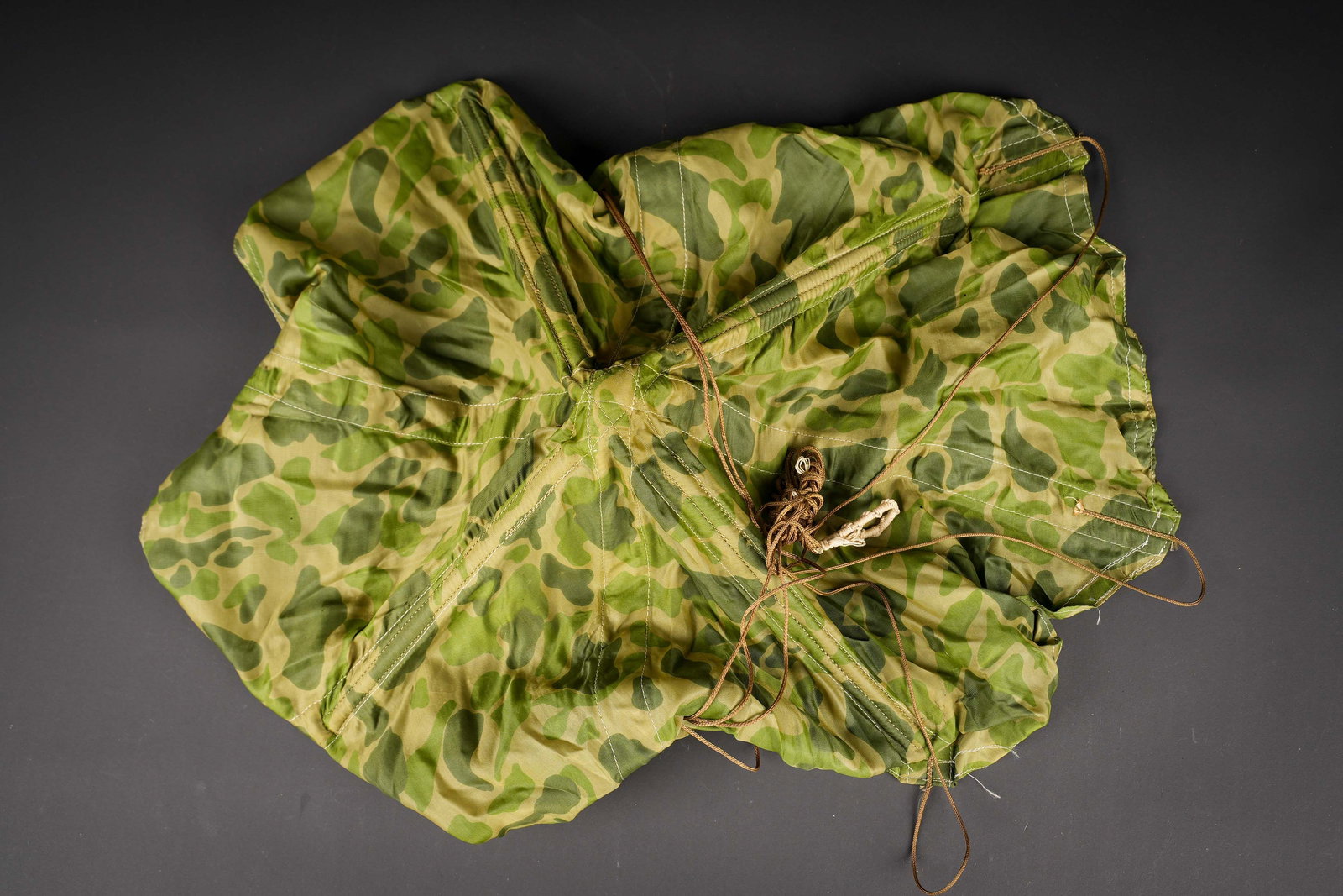 Extracteur de parachute US. US parachute ripcord handle.: Extracteur de parachute US. En toile camoufle. Armature en metal. Les suspentes sont presentes, ainsi que lanneau de fixation a la cheminee du parachute. Marquages Part NO 43K21909 MFG By Hightstown