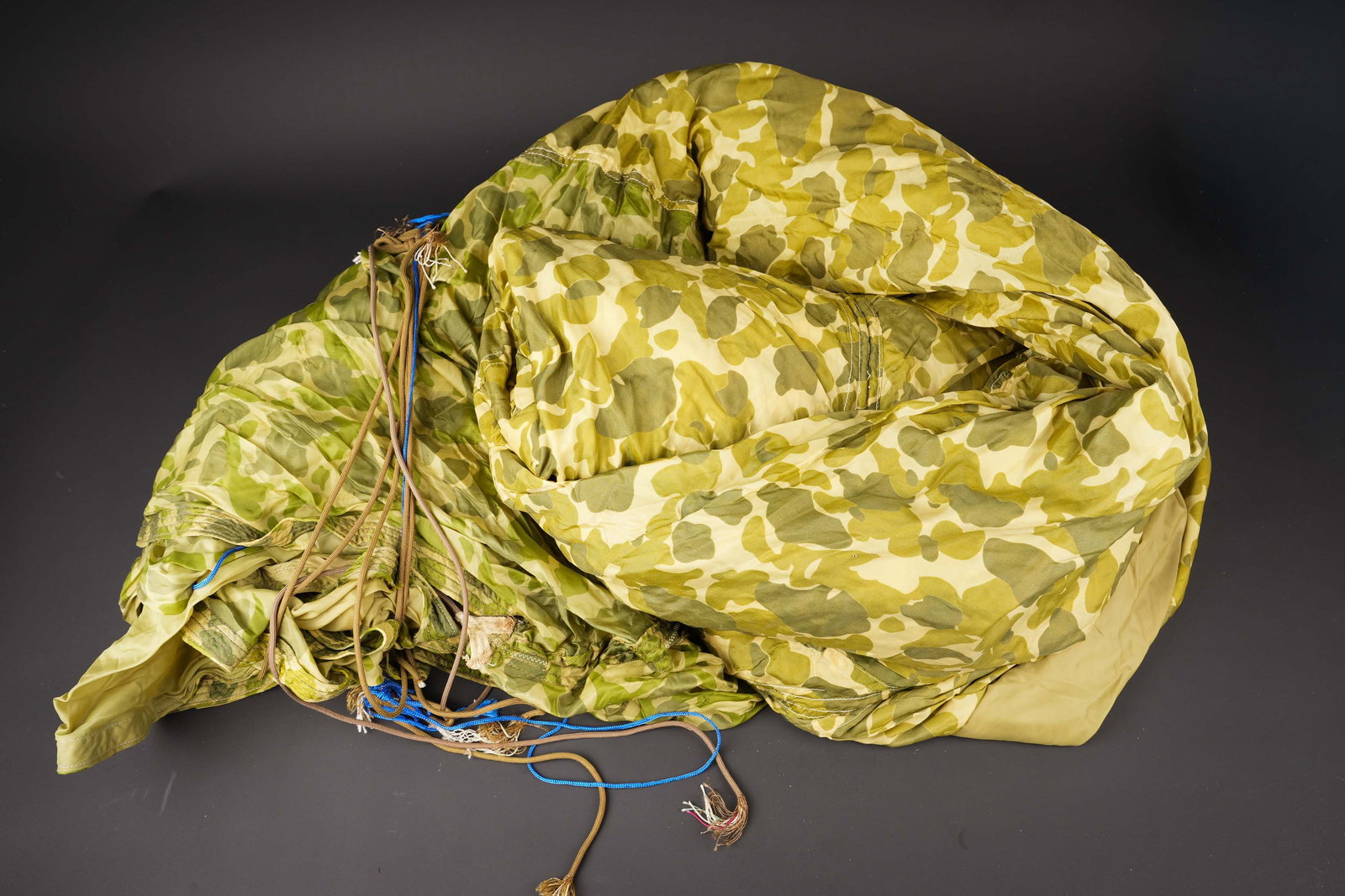 Voilure de parachute US. US parachute canopy.: Voilure de parachute US. En tissu camoufle. Nombreuses reparations avec divers modeles de voilures. Les suspentes sont coupees. 26 panneaux. Marquages Unsafe For Personnel July. A noter une certaine