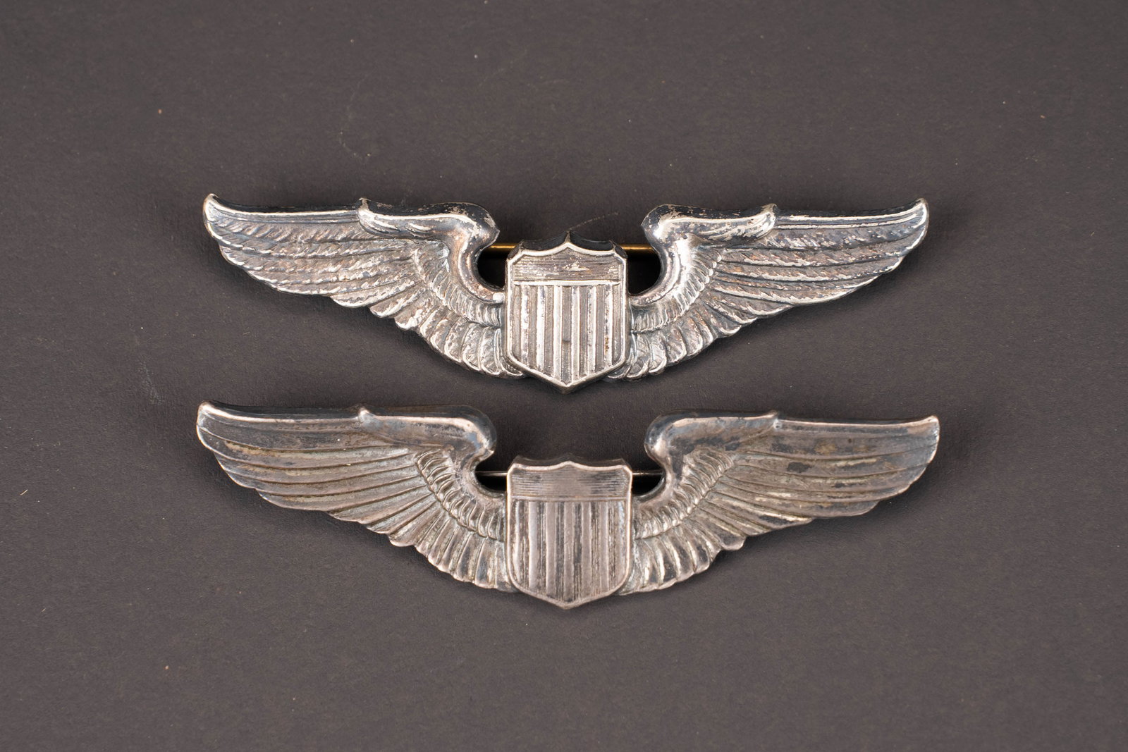 Brevets de pilote US. USAAF wings.: Brevets de pilote USAAF. Deux modeles differents de brevets de pilote en metal. Les attaches sont presentes. Un marquage est illisible, le second est marque Sterling. A noter une certaine usure et pat