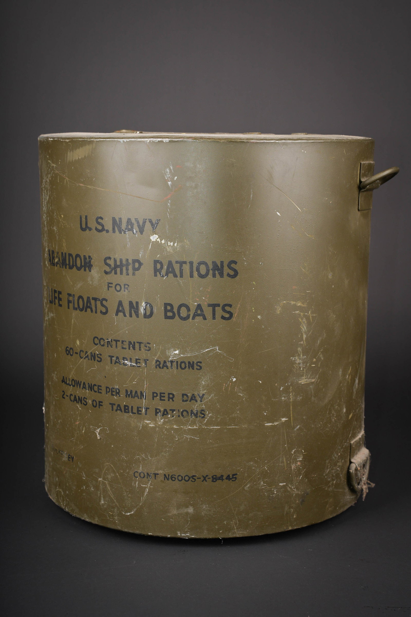 Container de survie US Navy. US Navy survival container.: Container de survie US Navy. Baril en metal. Peinture kaki a 70%. Les attaches laterales sont presentes. Les sangles sont manquantes. Marquages US Navy Abandon ship rations for life floats and boat co