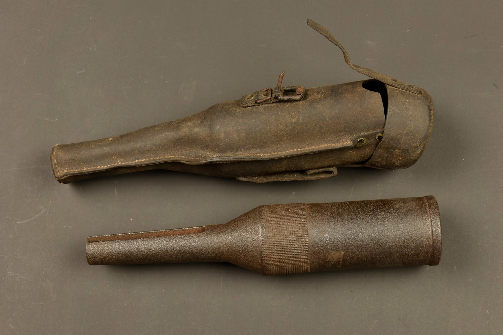 Tromblon VB avec son etui en cuir retourne. VB rifle grenade launcher with reversed leather carrier: Tromblon VB avec son etui en cuir retourne. Tromblon en fer, legerement oxyde, dans son rare etui en cuir retourne, complet de son passant, sangle et boucle de fermeture. Fabrication rivetee. Usure d 