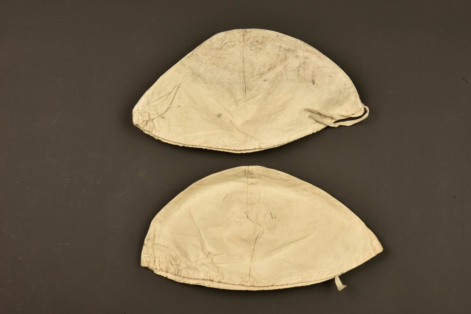 Lot de 2 couvres casque Adrian. Lot of two Adrian helmet covers: Lot de 2 couvres casque Adrian. Du modele de la Grande Guerre mais fabriques entre deux guerres, realises en 2 pieces de tissus reunies par couture avec ruban plat de serrage. En calicot blanc dont un