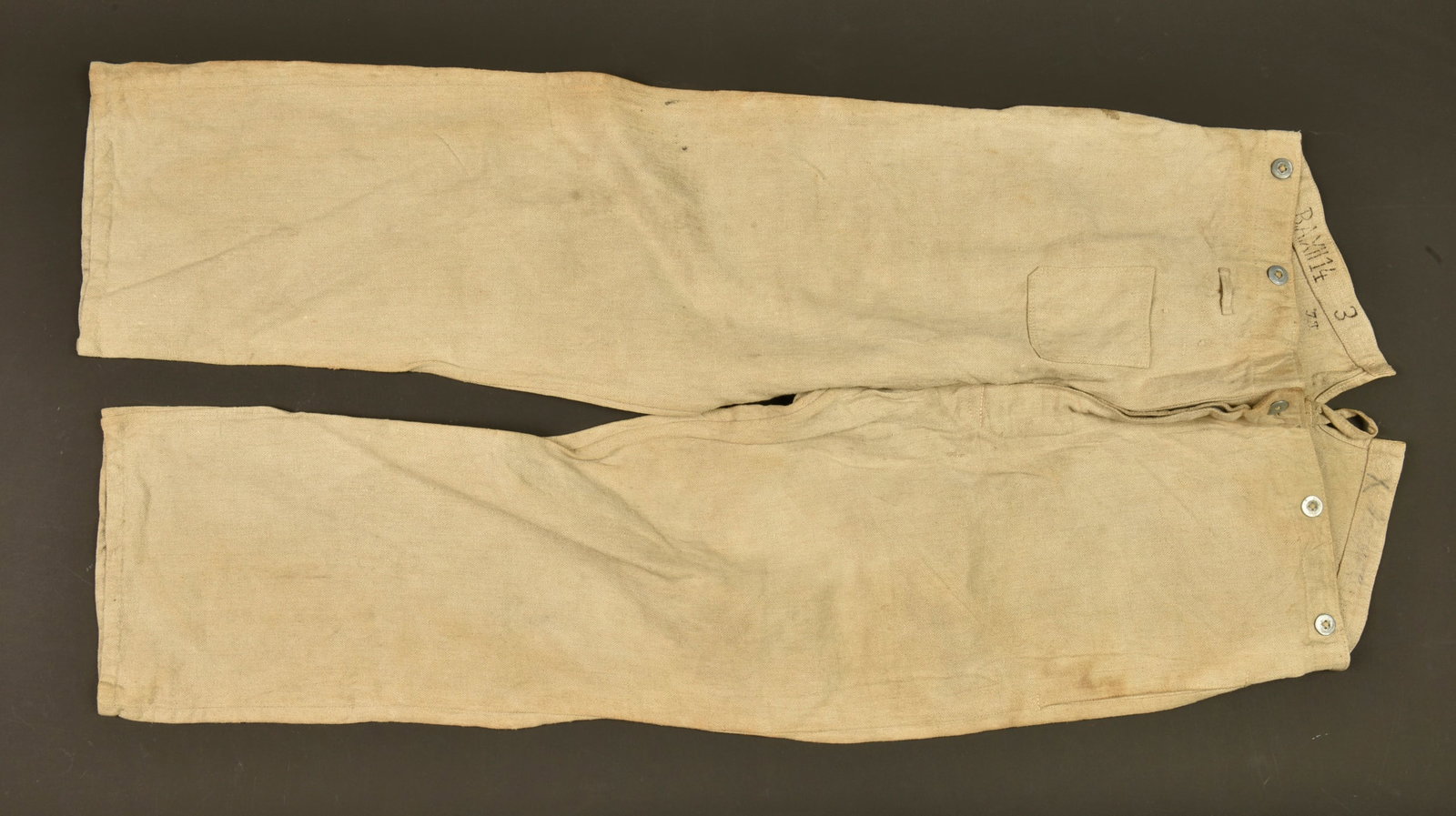 Pantalon de travail saxon du BA XII. Saxon work trousers from Bekleidungsamt XII: Pantalon de travail saxon du BA XII. En treillis chevron ecru, avec poche de gousset, tampon du BA XII 1914, inscription manuscrite illisible. Avec sa martingale et ses boutons. En bel etat, quelques 