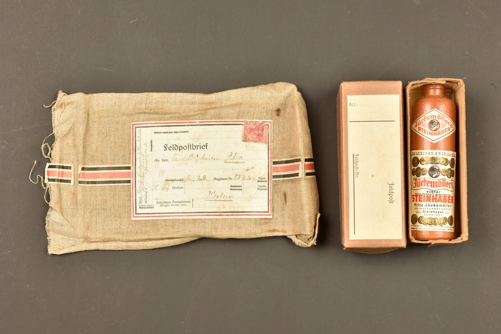 Lot colis Feldpost allemand. Lot of German Feldpost parcels: Lot colis Feldpost allemand. Comprenant un petit colis Feldpost en carton, etiquette vierge, contenant une miniature de bouteille Steinhager en gres avec etiquette, et une etiquette Feldpost sur parti
