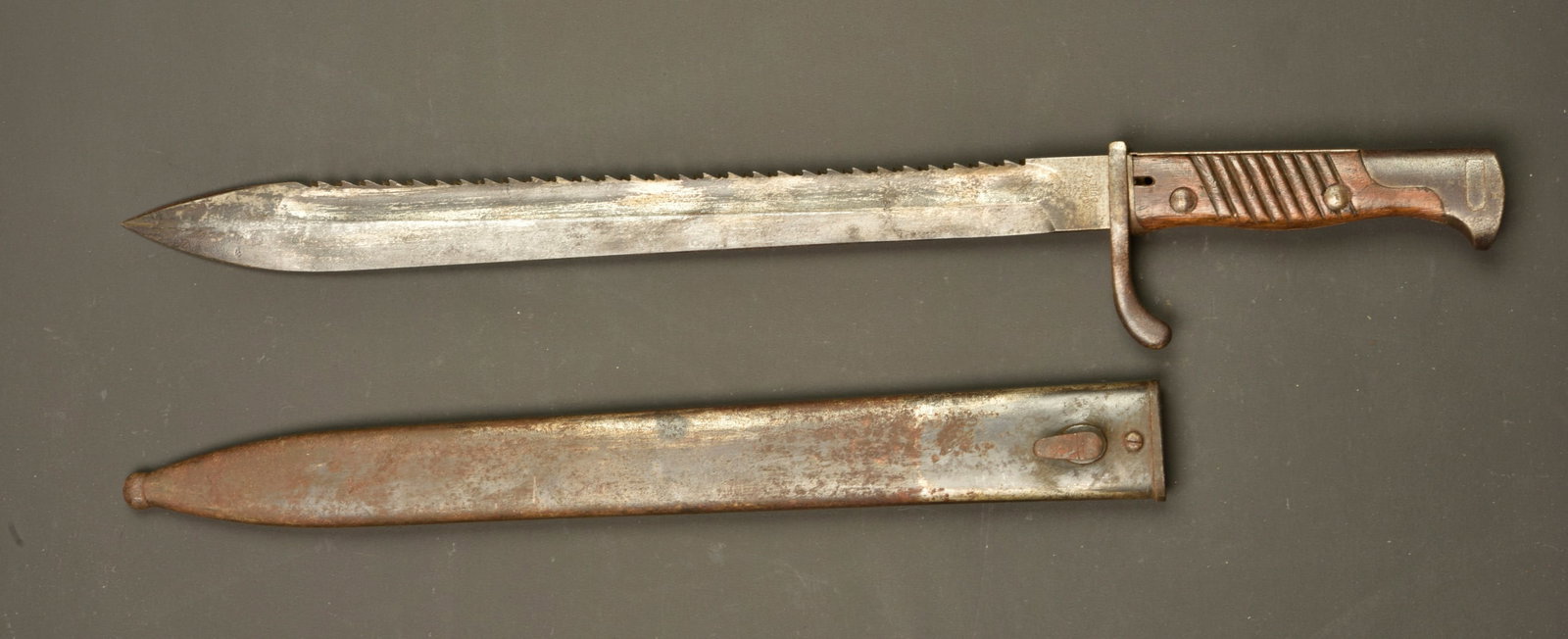 Baionnette allemande 98-05 dents de scie. German 98/05 sawback bayonet: Baionnette allemande 98-05 dents de scie. Lame datee 1915 du fabricant C.G. HAENEL de Suhl, oxydation superficielle. Plaquettes bois striees. Bouton ressort fonctionnel. Fourreau fer. Usure d usage, p