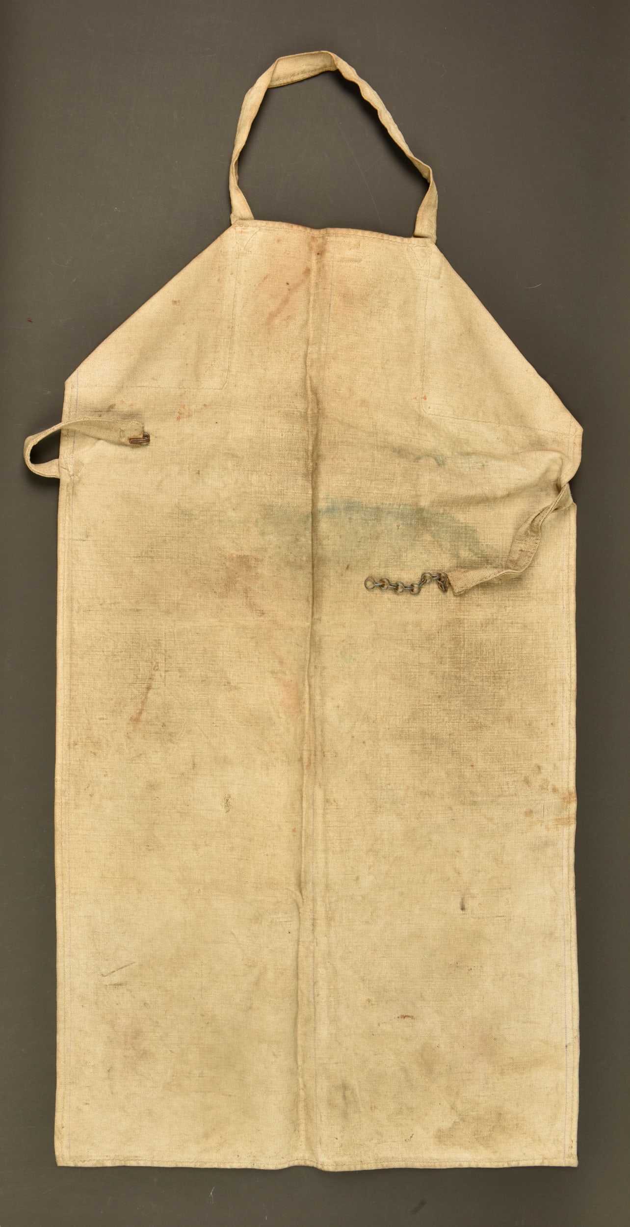 Tablier de travail allemand avec etiquette mitrailleur. German work apron with machine gunner label: Tablier de travail allemand avec etiquette mitrailleur. Tablier en forte toile ecrue, avec sangle de cou et ceinture de fermeture a chainette et crochet. Etiquette nominative periode Reichswehr ou Rei
