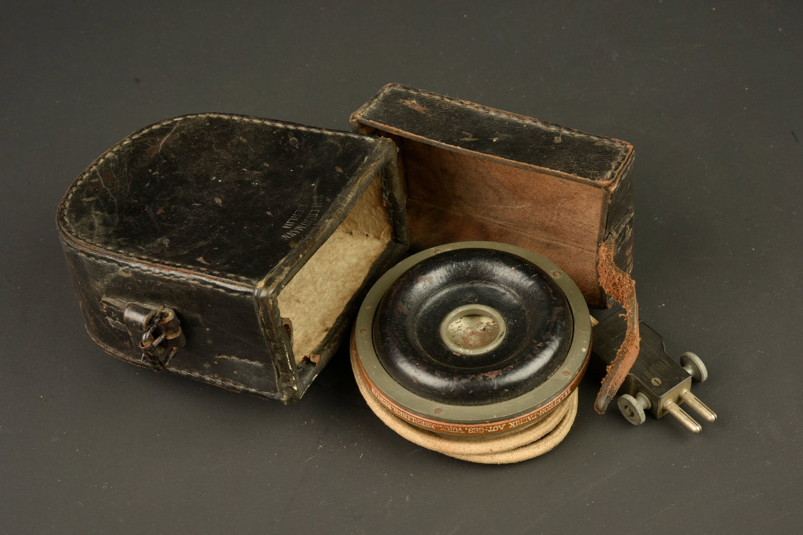 Ecouteur telephonique allemand dans son etui cuir. German telephone receiver in its leather case: Ecouteur telephonique allemand dans son etui cuir. Tres bel ecouteur, en superbe etat, avec son cable et sa fiche. Dans un etui en cuir fonce, fabricant Hartmann Berlin, avec sa sangle de fermeture. U