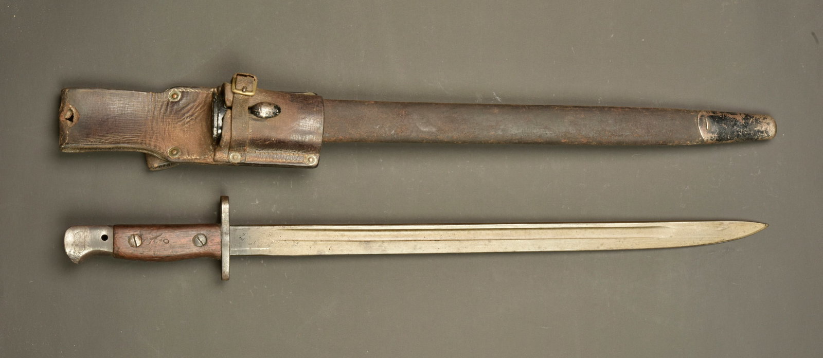 Baionnette anglaise 1907 avec porte fourreau cuir. British Pattern 1907 bayonet with leather frog: Baionnette anglaise 1907 avec porte fourreau cuir. Lame du fabricant Wilkinson date illisible sous poincon d inspection. Plaquettes bois. Bouton ressort fonctionnel. Fourreau cuir et fer. Porte