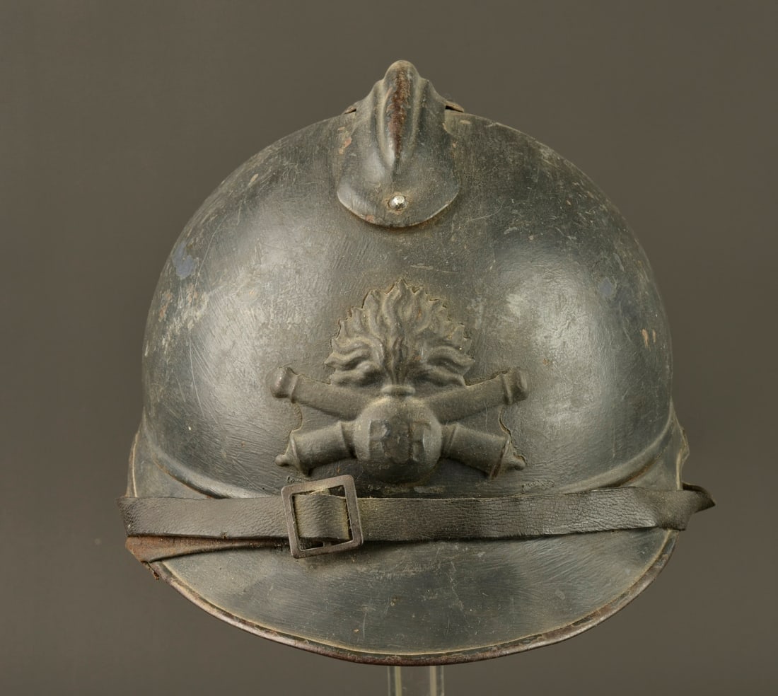Casque Adrian 1915 artillerie. Model 1915 Adrian helmet for artillery.: Casque Adrian 1915 artillerie. Casque modele 1915 en peinture bleu horizon recouverte d une peinture plus foncee au pinceau. Attribut modele 1915 de l artillerie, jugulaire en cuir presente mais avec 