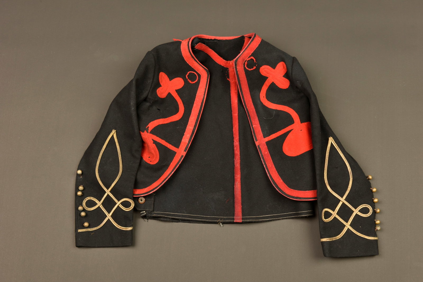 Gilet bolero zouave enfant. Child’s Zouave bolero waistcoat.: Gilet bolero zouave enfant. Un gilet en fin drap noir, parements ecarlates se refermant par trois crochets aux epaules et trois boutons lateraux. Bolero en drap noir, parements en drap ecarlate, tombe