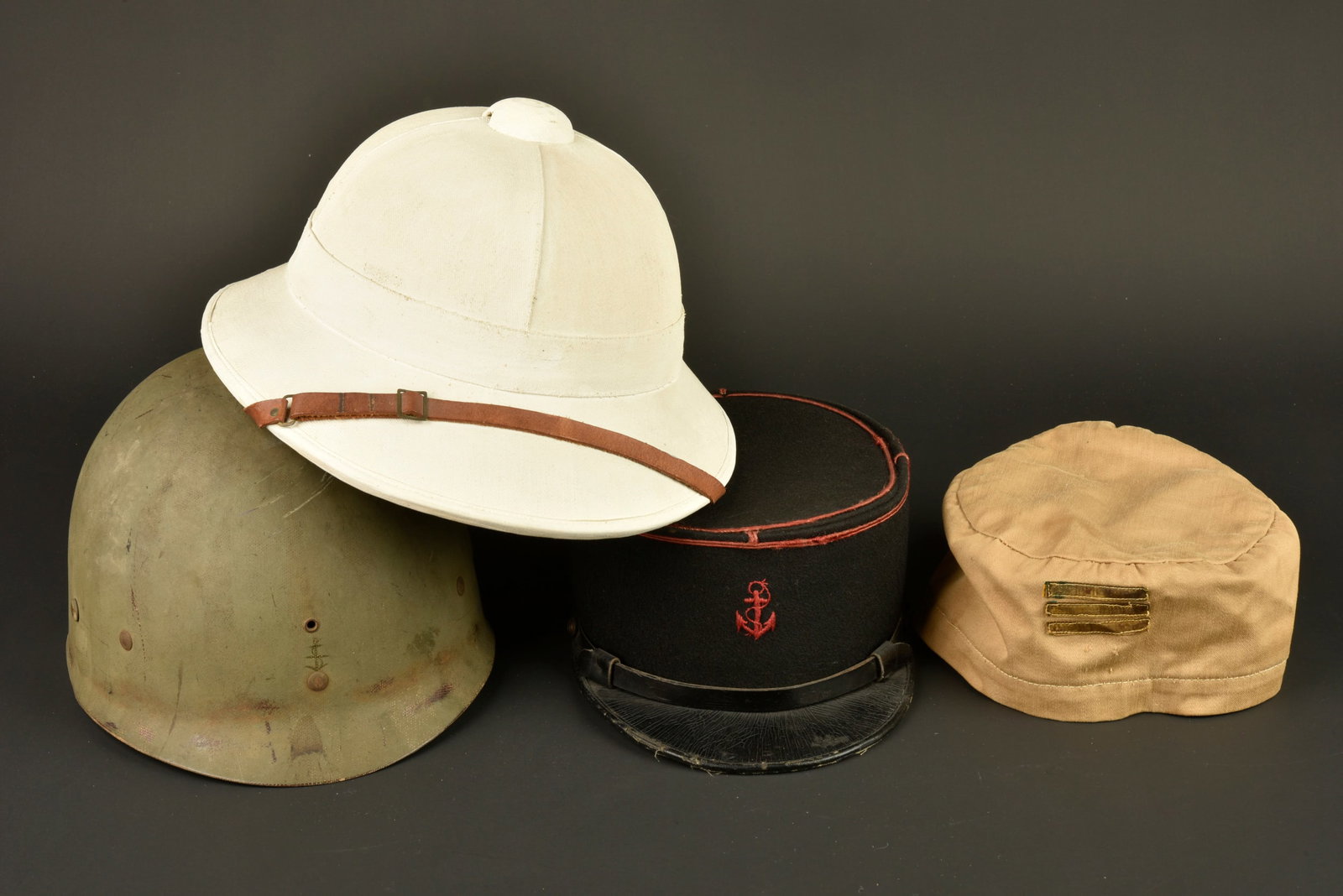 Ensemble de coiffures coloniales. Set of colonial headdress.: Ensemble de coiffures coloniales. Comprenant un kepi modele 1935 d un marsouin confectionne en drap bleu fonce, passepoil ecarlate, ancre brodee au fil de coton ecarlate. Fausse jugulaire en fin cuir 