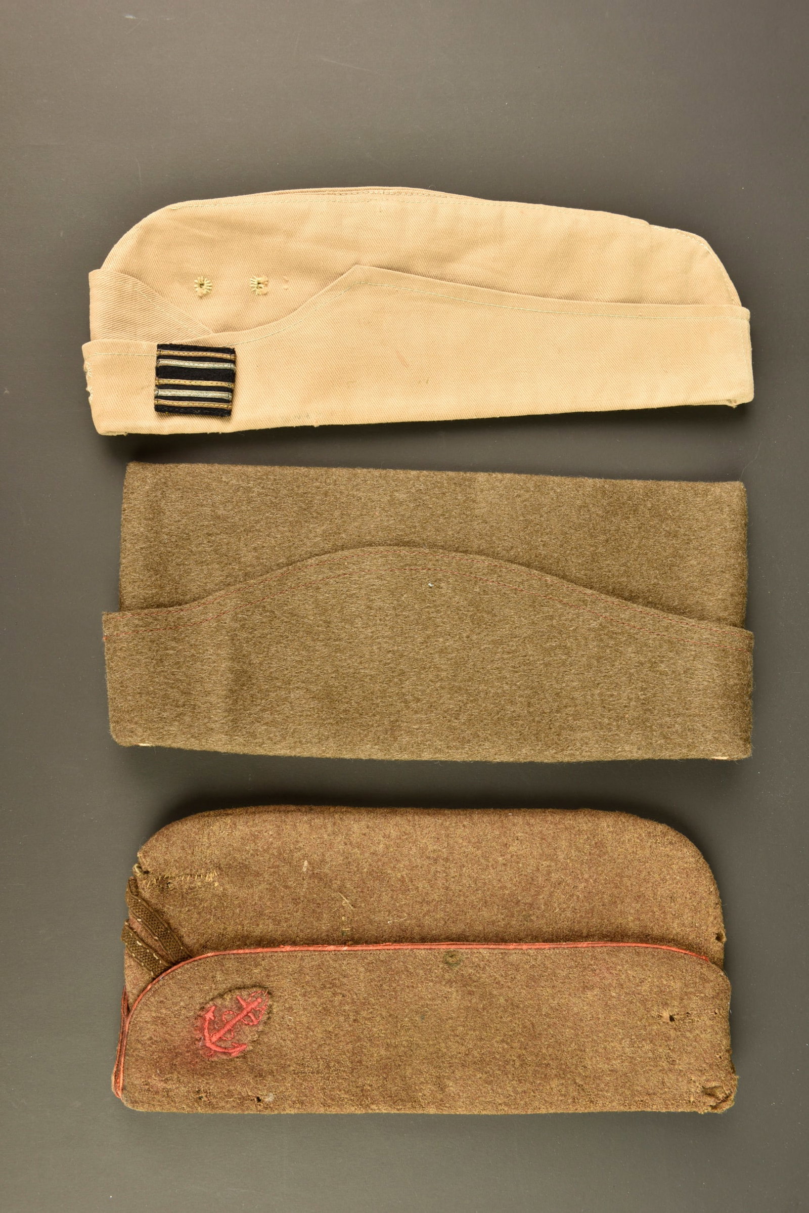 Ensemble de bonnets de police. Grouping of side caps.: Ensemble de bonnets de police. Comprenant un bonnet de police modele 1935 troupe en drap kaki, doublure en coton ecru portant le tampon de taille 59 ainsi qu un tampon de fabricant et celui du collect