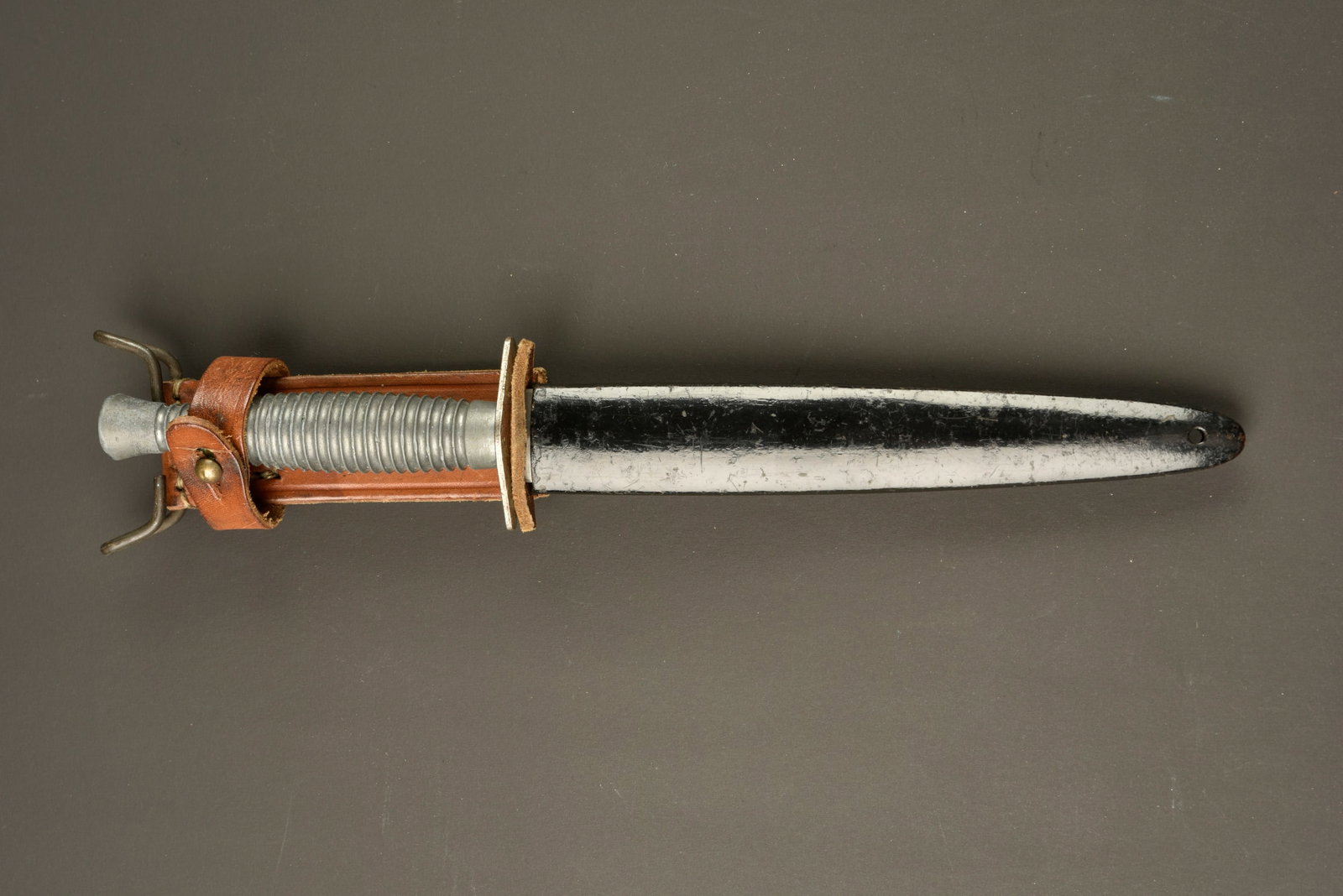 Dague Le Commando. Le Commando dagger.: Dague Le Commando dite FOM. Poignee moulee en zamak gris comportant 26 cannelures. Garde d origine droite surmontee d une protection en cuir. Vis de demontage d origine. Lame dans sa longueur d origin