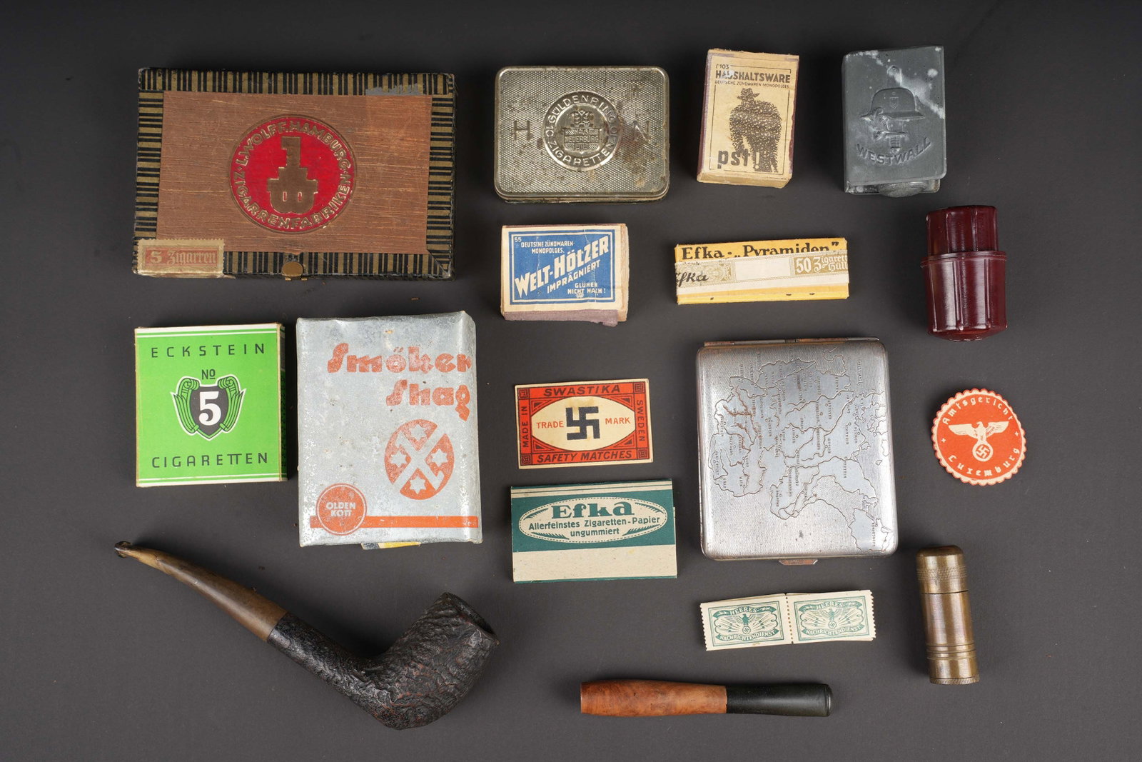 Accessoires du fumeur allemand. German smoker accessories.: Accessoires du fumeur allemand. Comprenant un paquet jamais ouvert de tabac Smoker Shag. Une boite en contre plaquee, marquee L Wolff Hamburg. Une boite de cigarette en metal couleur argent. Une