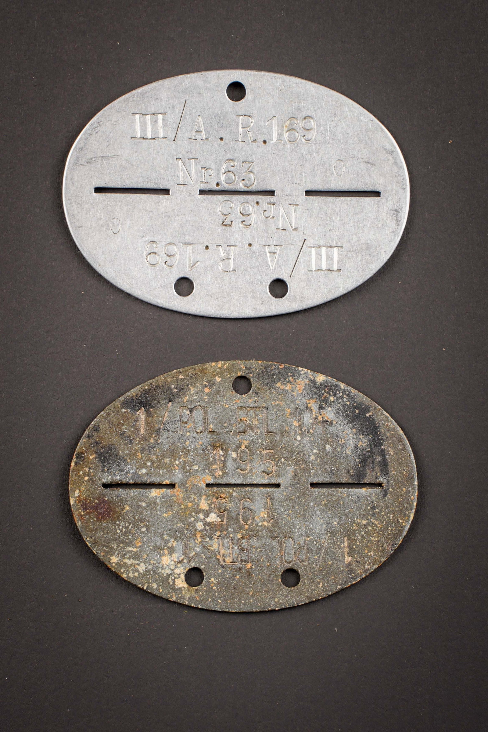 Plaques d identite allemande. German dog tags.: Plaques d identite allemande. Comprenant une plaque complete en aluminium, marquee III/A.R.169 NR 63, groupe sanguin O. Une plaque d identite en metal, partiellement oxydee, marquee 1/POL. BTL. 104