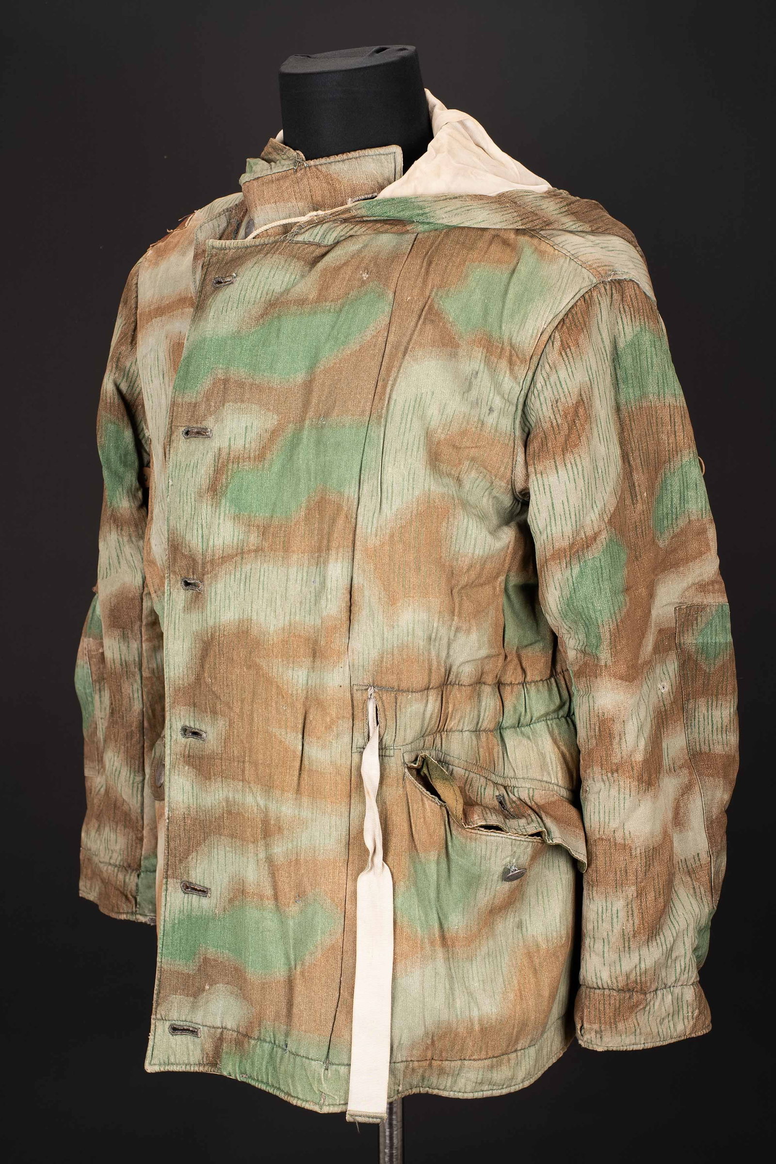 Parka reversible allemande. Reversible German parka.: Parka reversible allemande. En tissu camoufle eclat, fortement use et decolore par le soleil. La majorite des boutons sont presents. Reversible blanc. Les cordons de serrage sont presents. Les marquag
