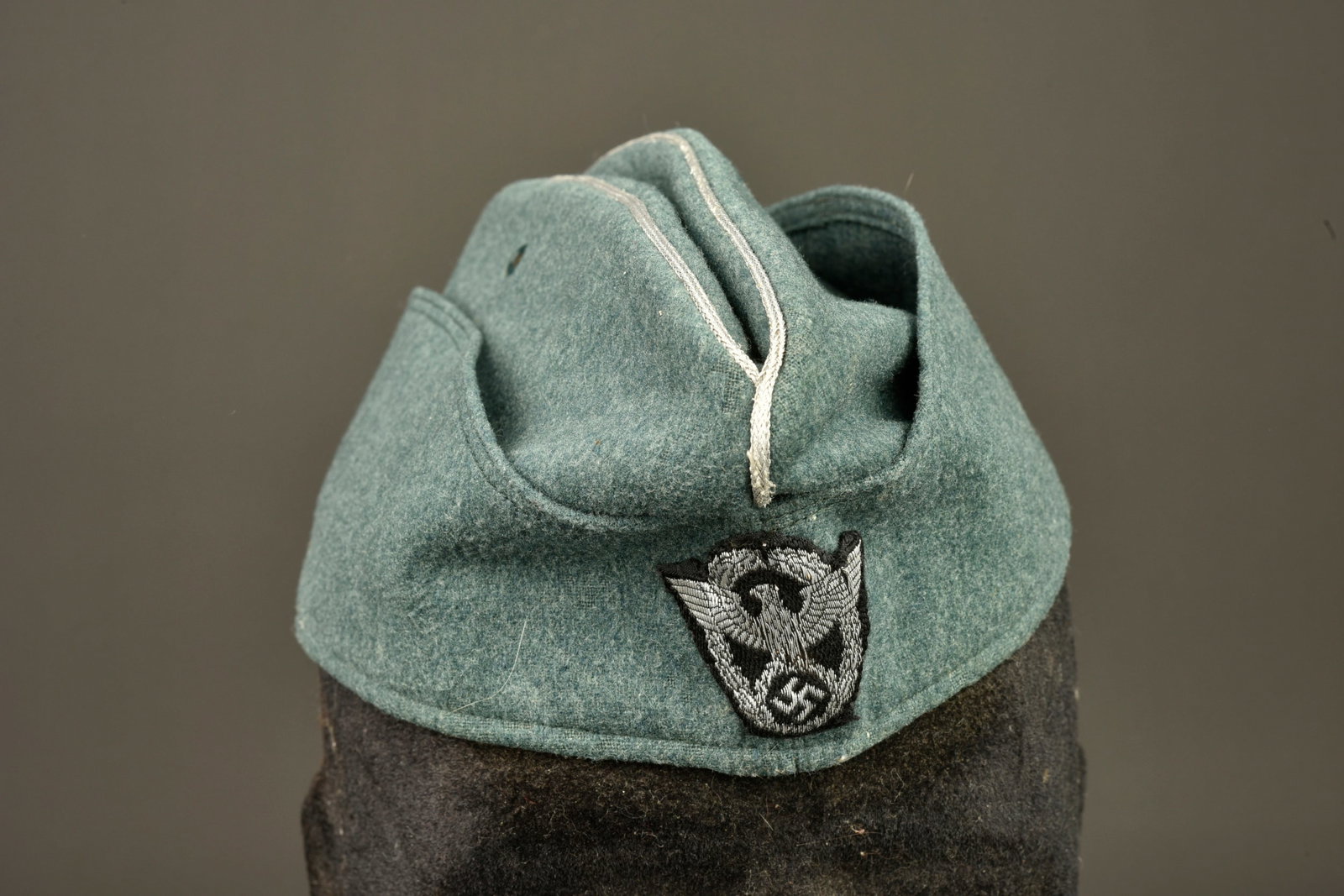 Calot officier Polizei. Officer Police garrison cap.: Calot d officier Polizei. En drap gris/vert. Deux ?illets d aeration en couleur d origine. Lisere argent faisant le tour de la coiffure. Insigne Bevo sur fond noir, cousu main. Interieur double en