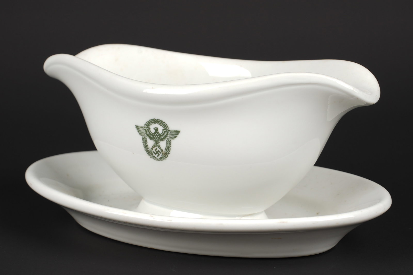 Sauciere Polizei. Polizei sauce boat.: Sauciere Polizei. En ceramique blanche. Bel insigne Polizei imprime sur la face avant. Logo du fabricant visible, date 1941. Longueur environ 28 cm. A noter une certaine usure et patine de la piece. L