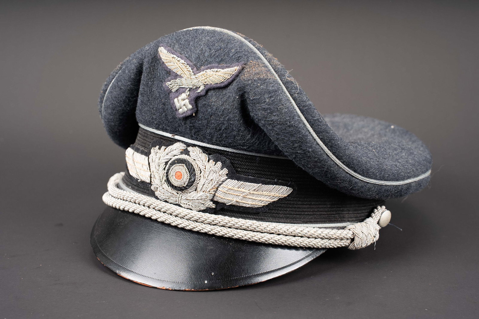 Casquette officier Luftwaffe. Luftwaffe officer?s visor cap.: Casquette d officier de la Luftwaffe. En drap gris bleu. Triple lisere argent. Bandeau en mohair noir. Jugulaire d officier. Insignes en cannetille argent. Interieur double en satinette jaune.