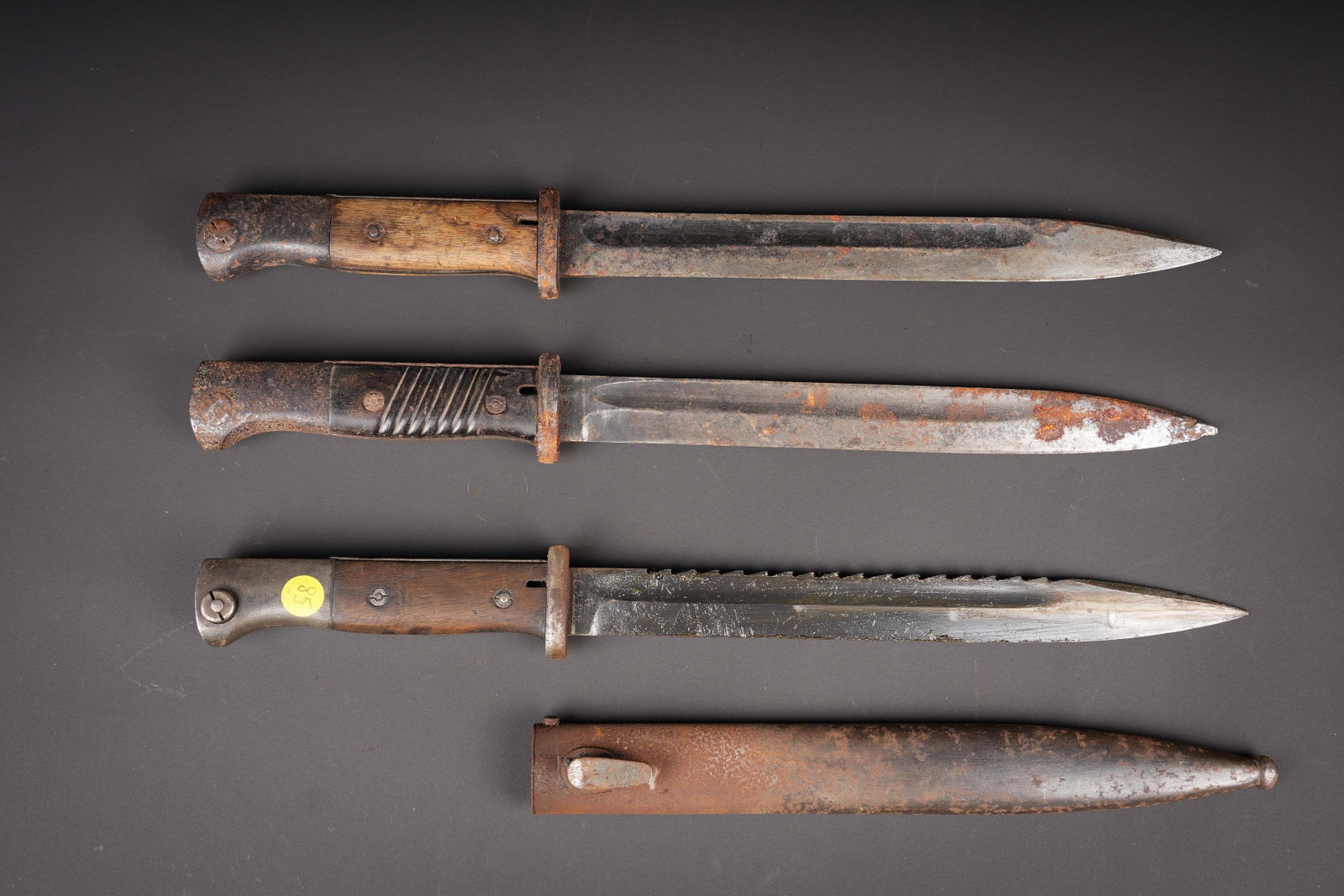 Lot de 3 baonnettes 98K. German 98K bayonets.: Lot de 3 baonnettes 98K. Une baonnette plaquettes bois, datee 1936, lame avec dents de scie post-war. Fourreau fer numero different. Deux baonnettes sans fourreau a nettoyer. Usure, oxydation. Lot of