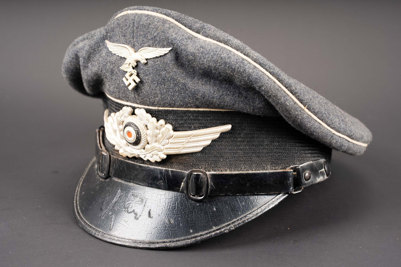 Casquette Hermann Goring. Hermann Goring visor cap.: Casquette de sous-officier des unites Hermann Goring. En drap gris bleu. Triple lisere blanc typique des unites Hermann Goring. Bandeau en mohair noir. Insignes metalliques. Aigle du premier type.
