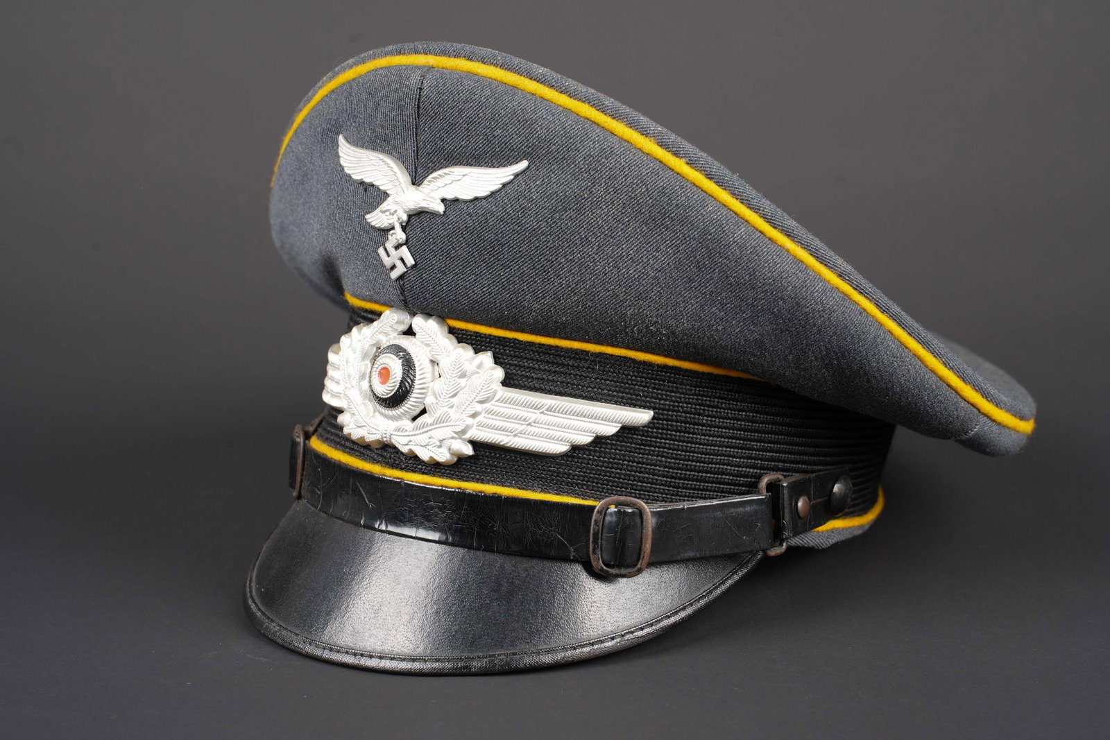 Casquette LW. German Luftwaffe visor cap: Casquette Luftwaffe. En gabardine gris/bleu. Triple lisere jaune du personnel volant ou parachutiste. Bandeau en mohair noir. Fausse jugulaire presente. Insignes metalliques. Les insignes n ont pas