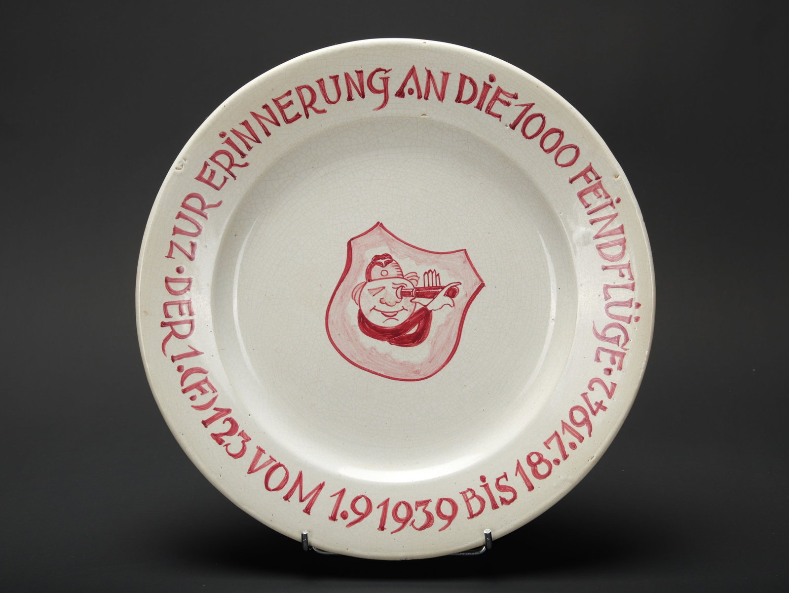 Plat du 1000eme vol du 1 F 123. JF 123 1,000th sortie commemorative plate.: Plat du 1000eme vol du 1 F 123. En ceramique, marquages sur le pourtour Zur Erinerrung an die 1000 Feindfluge Der 1 F 123 vom 1 9 1939 bis 18 7 1942. Modele d assiette se fixant au mur. Diametre 28,5 